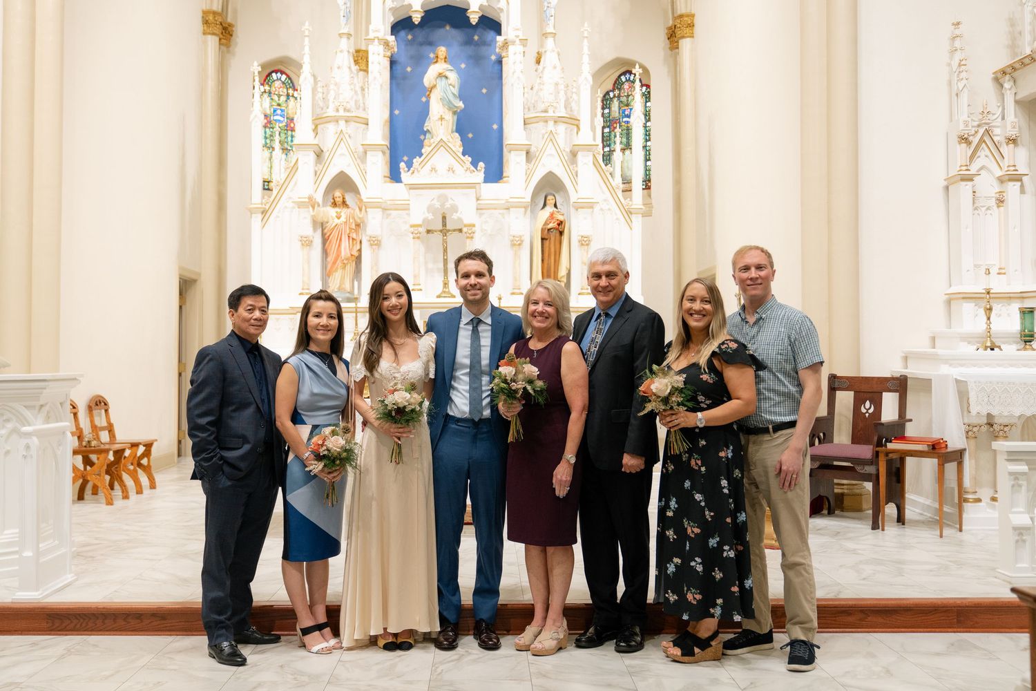 Small wedding group poses for photos inside a beautiful church with ornate altar and Gothic architecture.