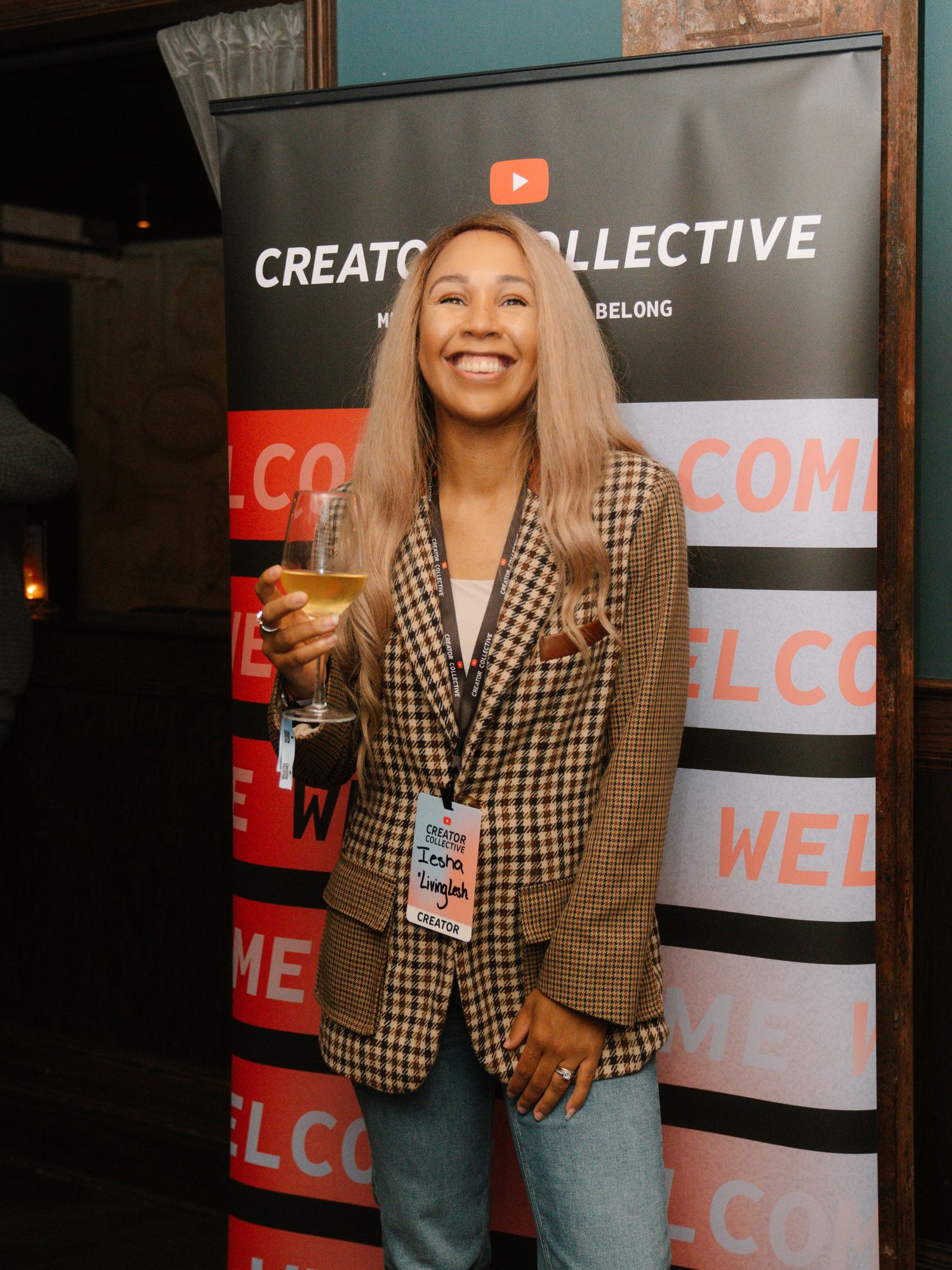 A person in a plaid blazer poses with champagne at a Creator Collective event.
