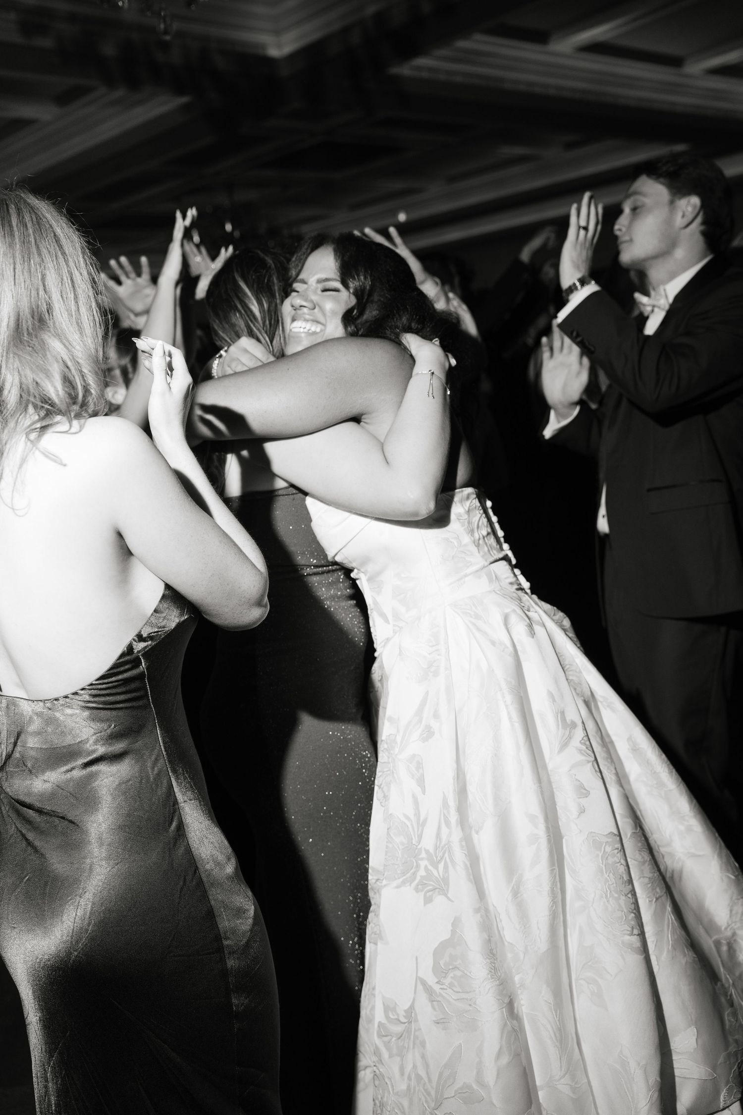 Bride joyfully hugs a guest on the dance floor during a lively black and white wedding reception.