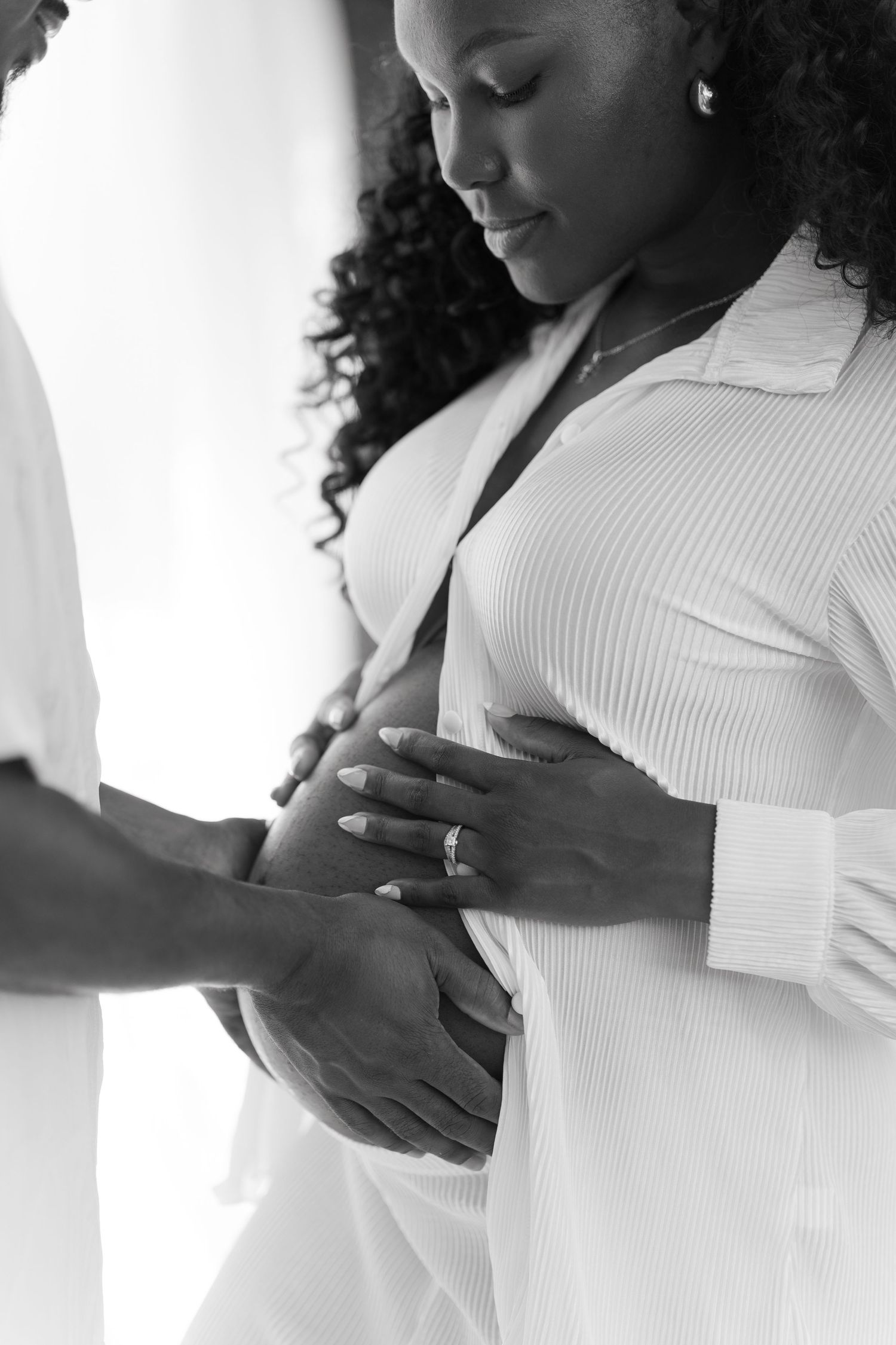 Black and white photo of a pregnant woman and partner tenderly holding her baby bump together.