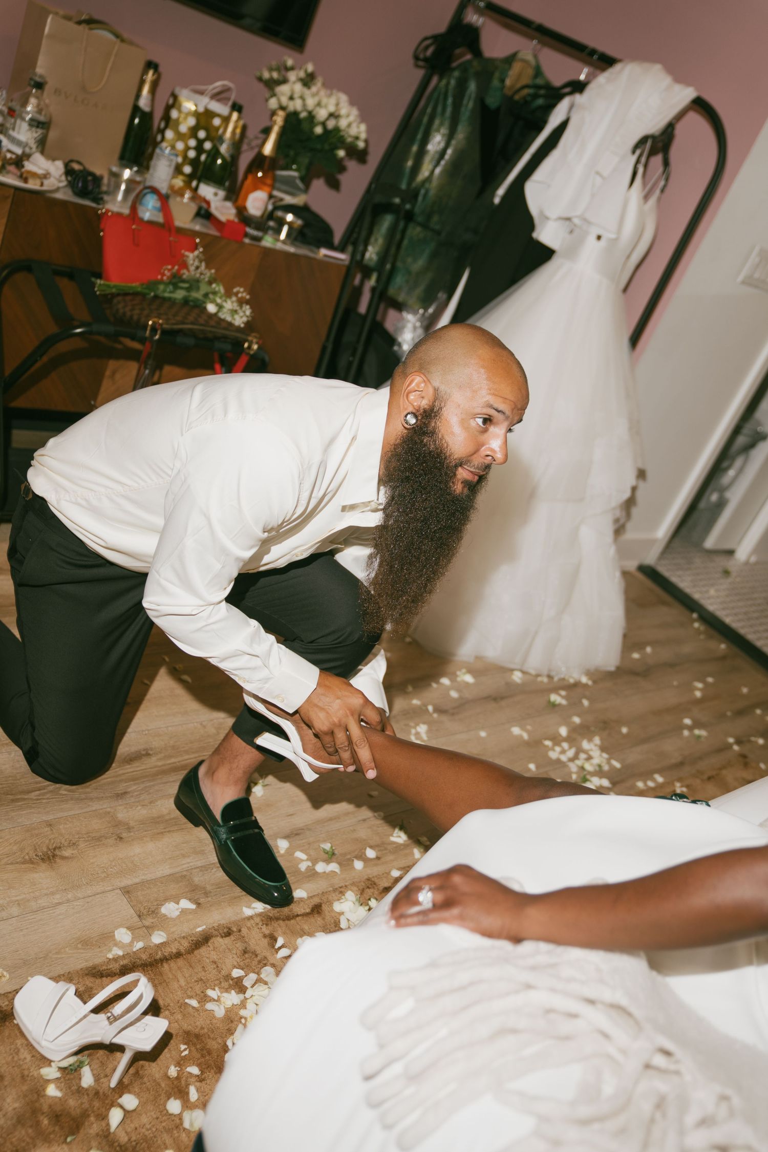 Candid moments between newlyweds on wooden floor with scattered flower petals.