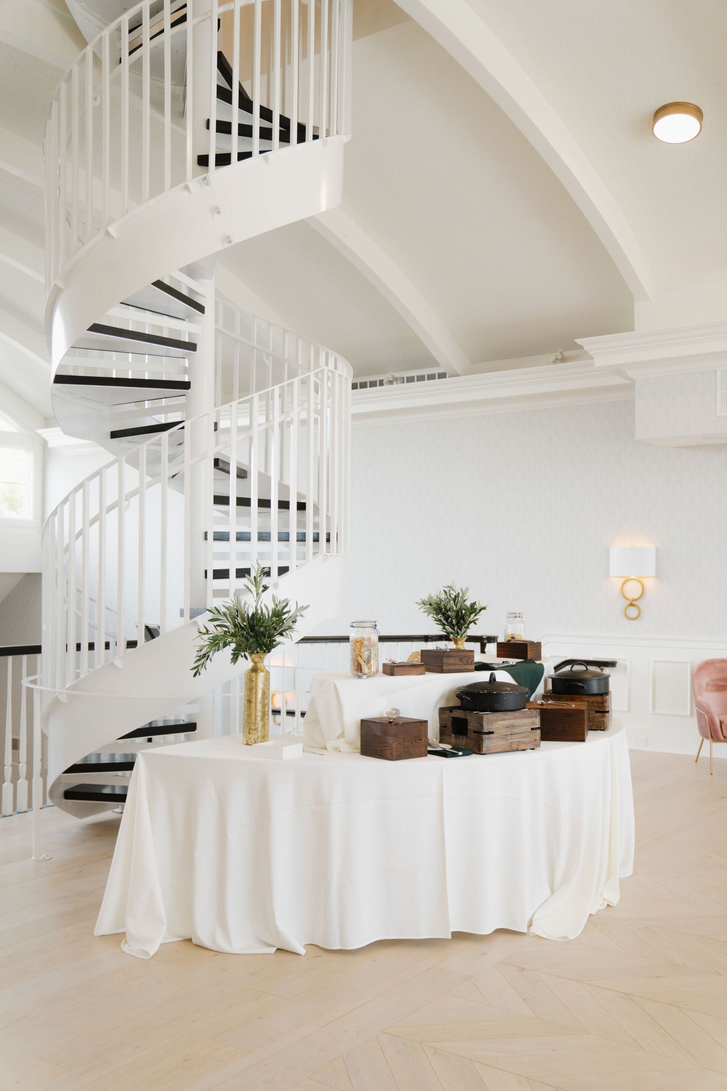 Elegant white spiral staircase and coffee service station with white tablecloth in a bright modern event space.