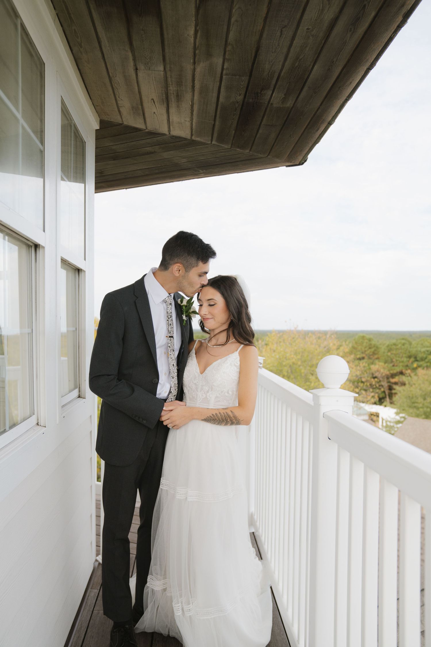 A romantic moment between newlyweds on a white porch overlooking scenic countryside.