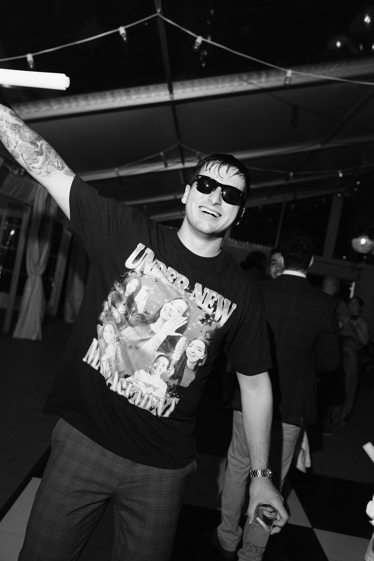 Black and white photo of party guests dancing in sunglasses and casual attire.