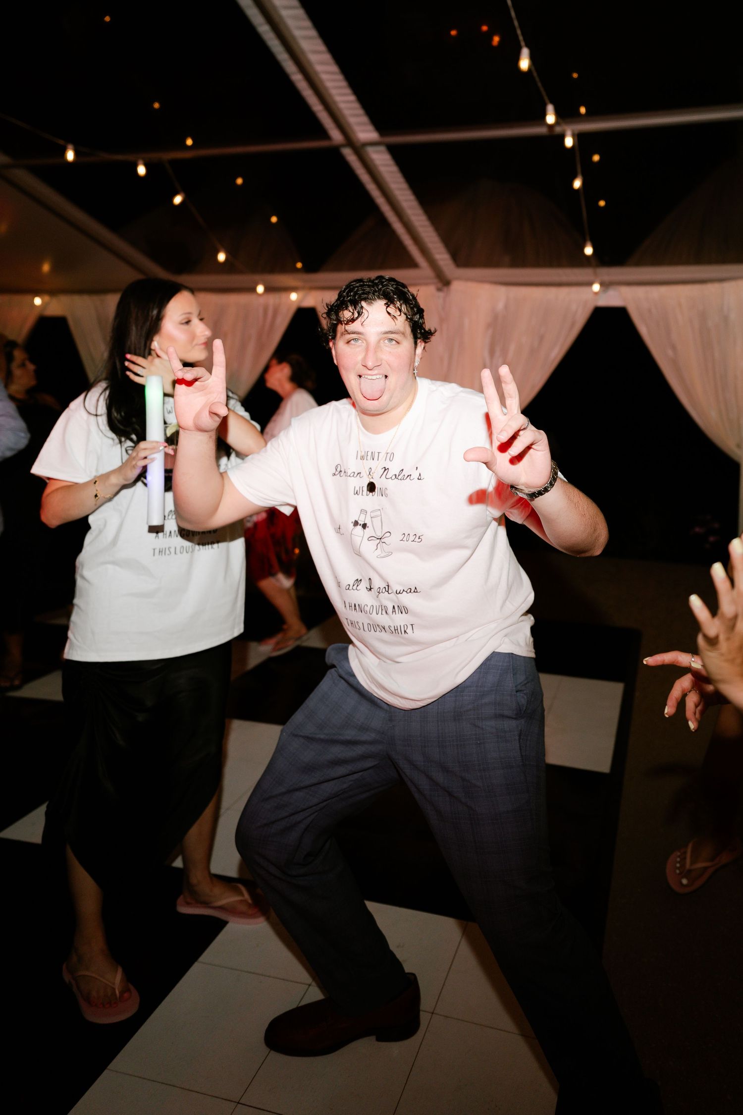 Wedding guests dancing energetically on checkered dance floor at night reception.