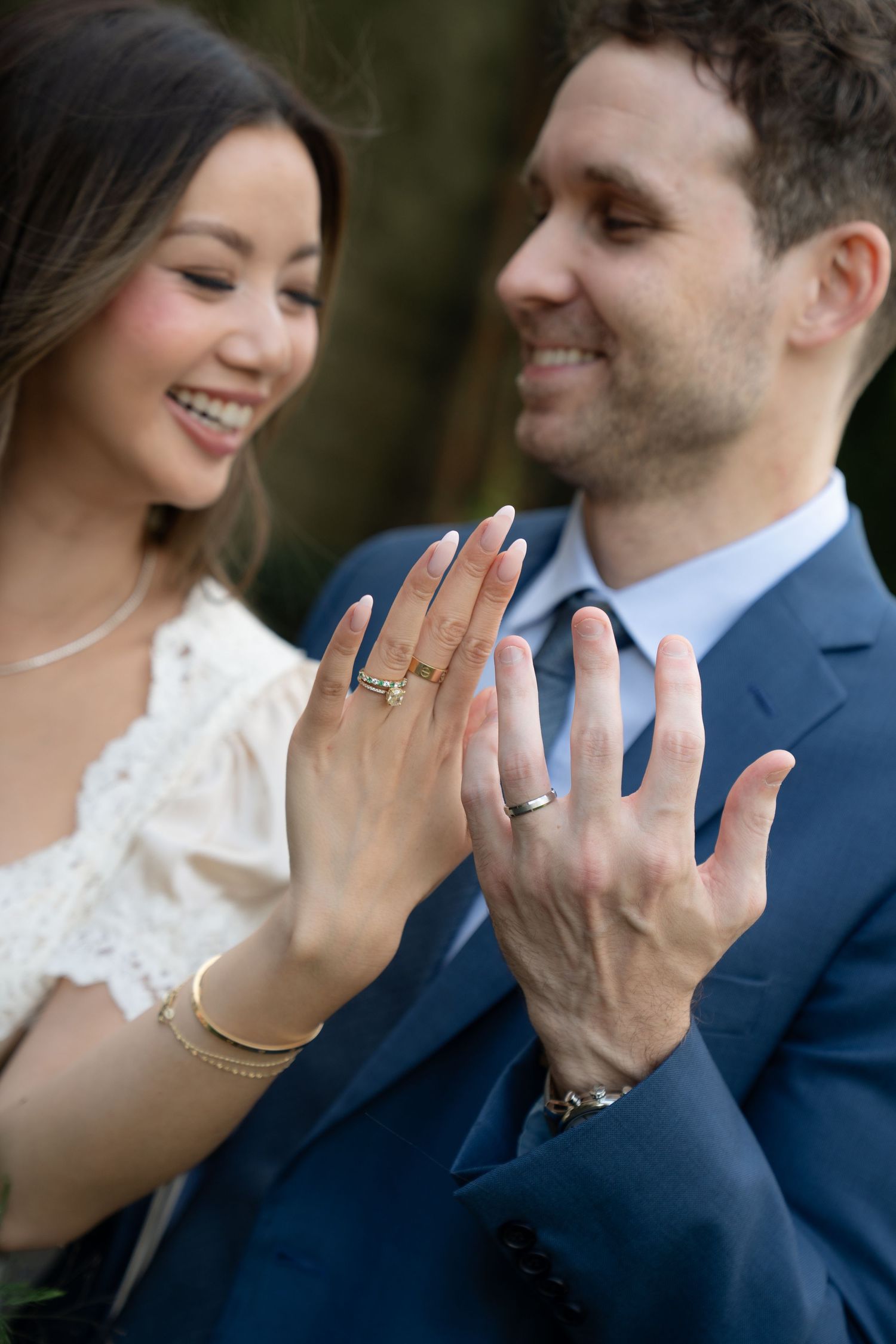 Close-up of hands showing wedding rings with joyful expressions in the background.