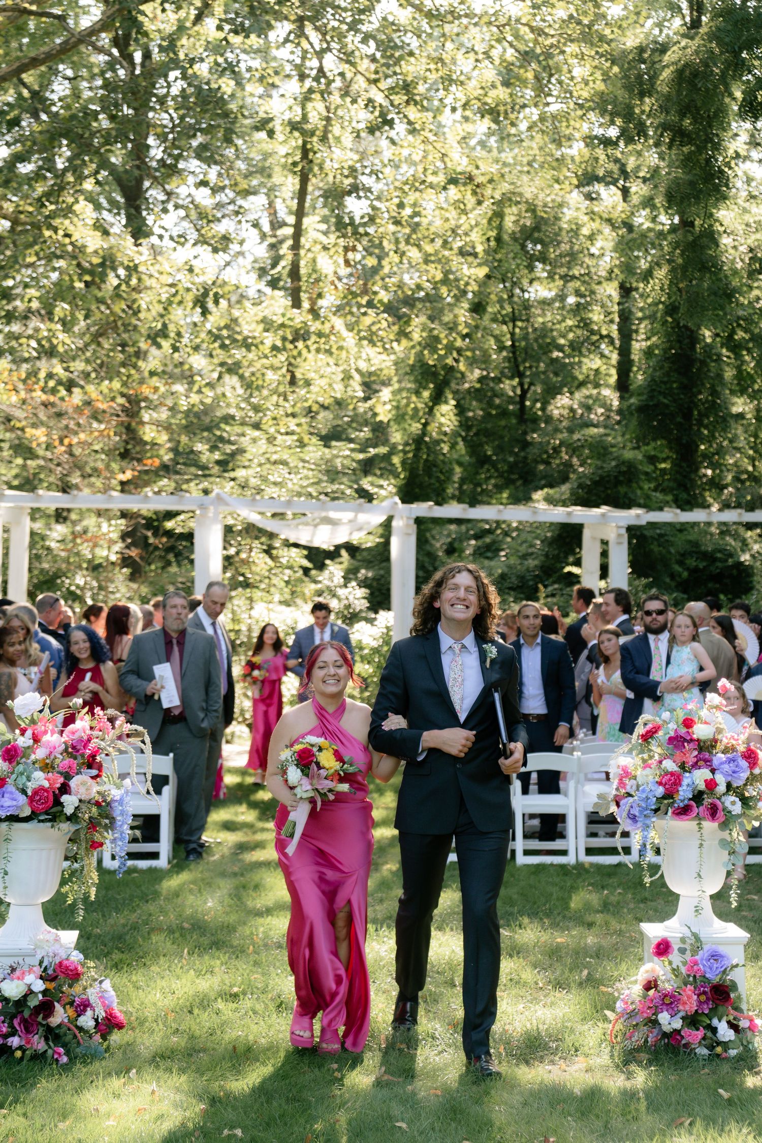 Garden wedding ceremony with pink floral arrangements and white chairs set up on a lawn.