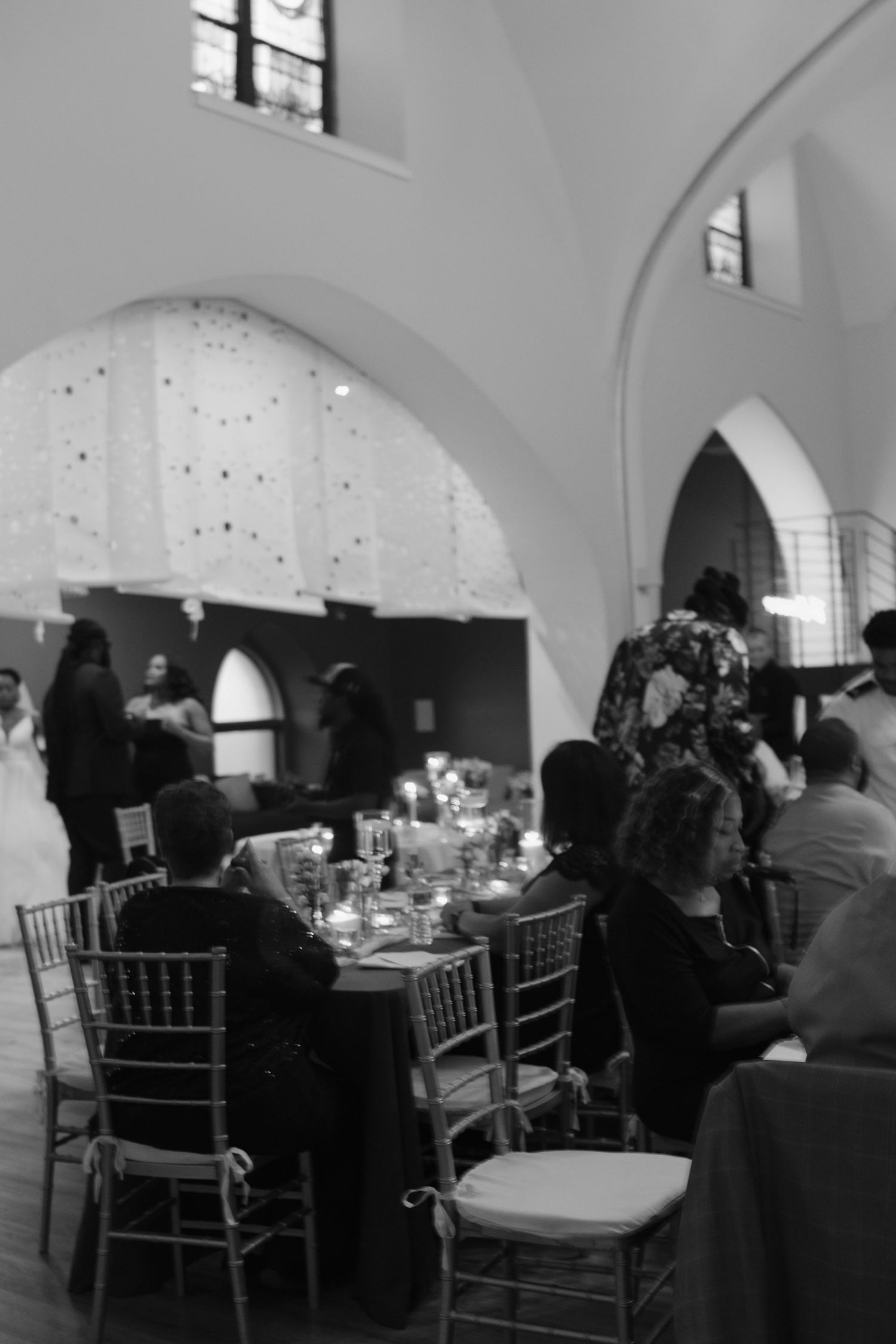 Wedding reception in an elegant arched venue with guests seated at formal dining tables.