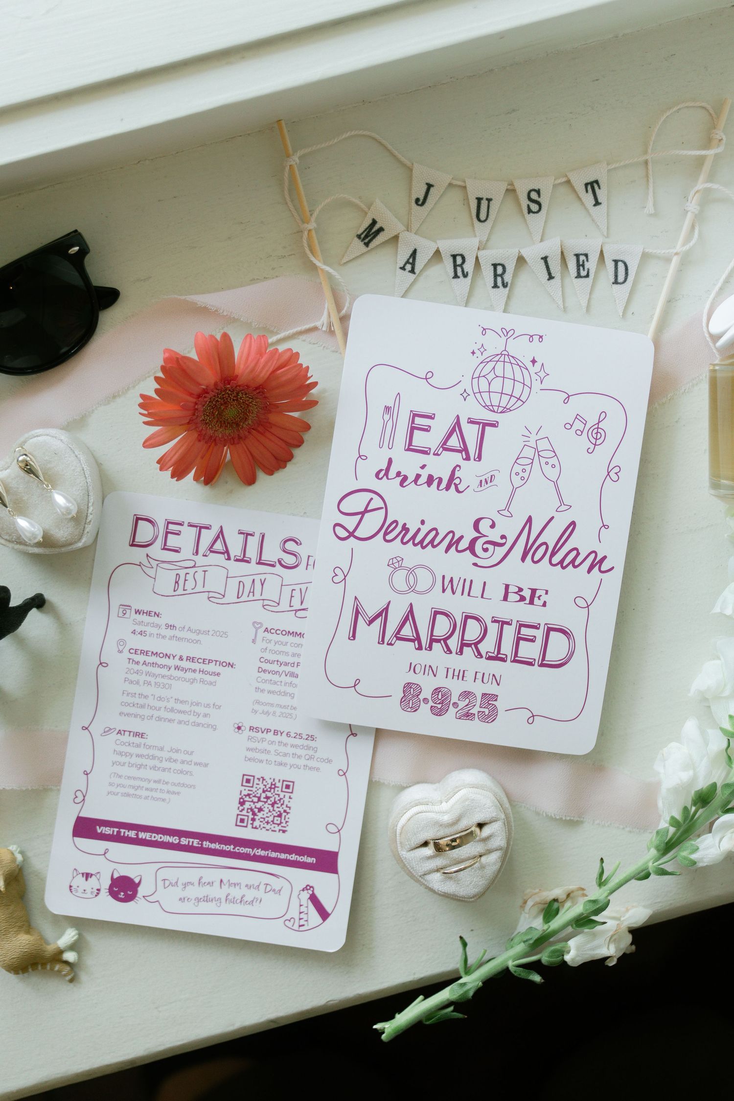 Wedding invitation suite with pink lettering and floral details displayed on white surface with a coral gerbera daisy.