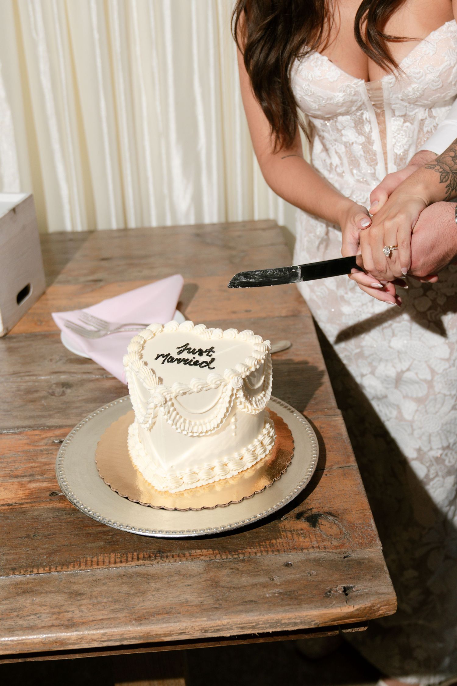 White wedding cake being cut on rustic wooden table with elegant decorative details.