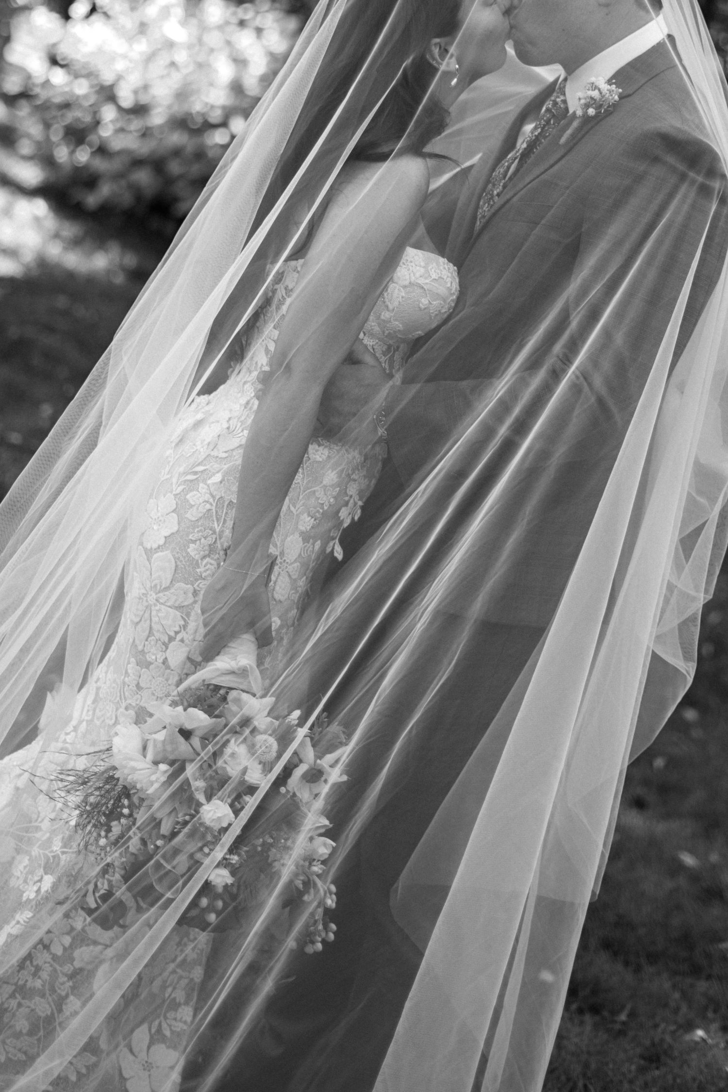 Black and white detail shot of a bride's lace dress and flowing veil.