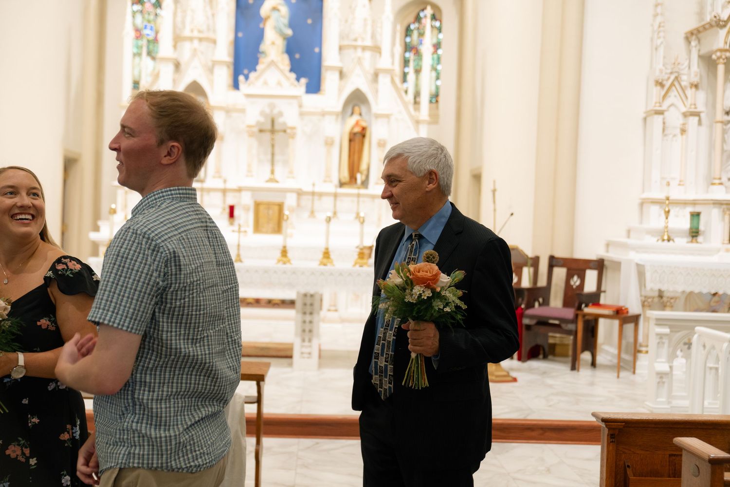 People gather inside a church with ornate altar decorations and religious statues in the background.