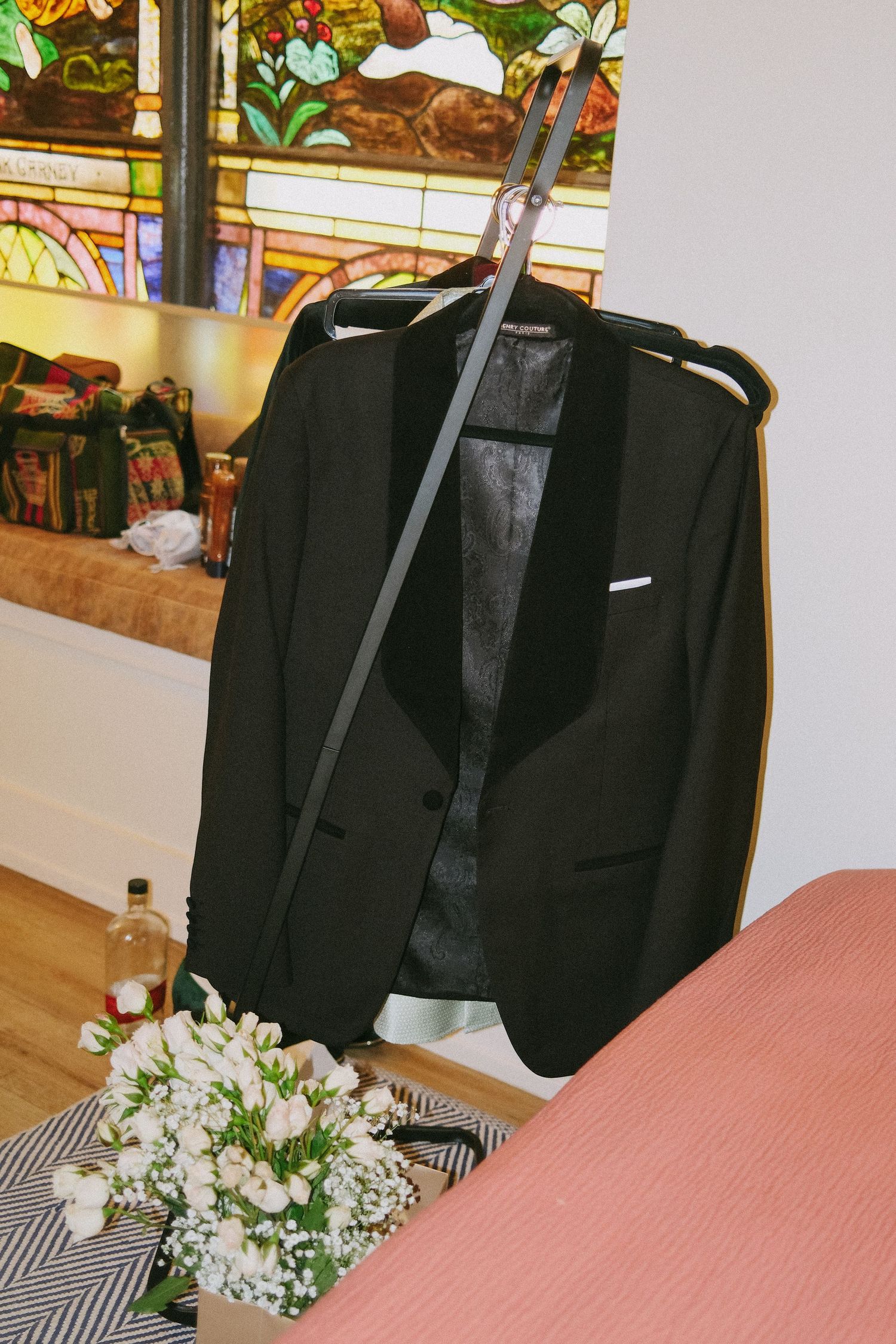 Black formal suit jacket hanging with white floral arrangements on a pink surface.