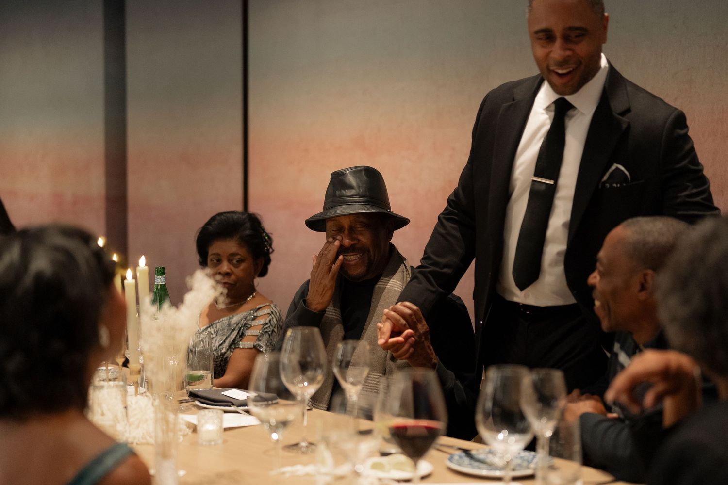 Dimly lit formal dinner gathering with guests seated at tables with candlelight.
