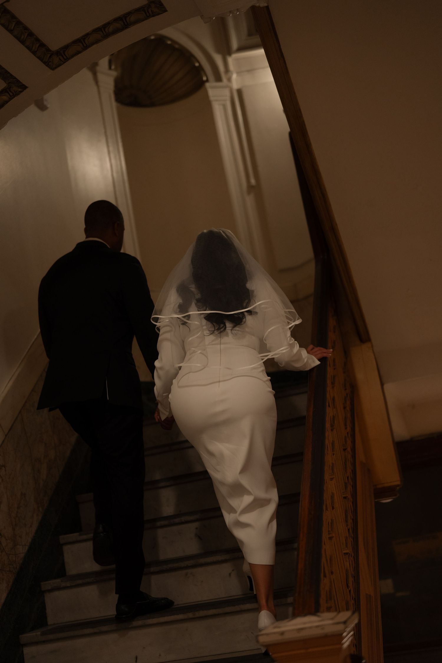 A couple ascending marble stairs with the bride wearing a white dress and veil.