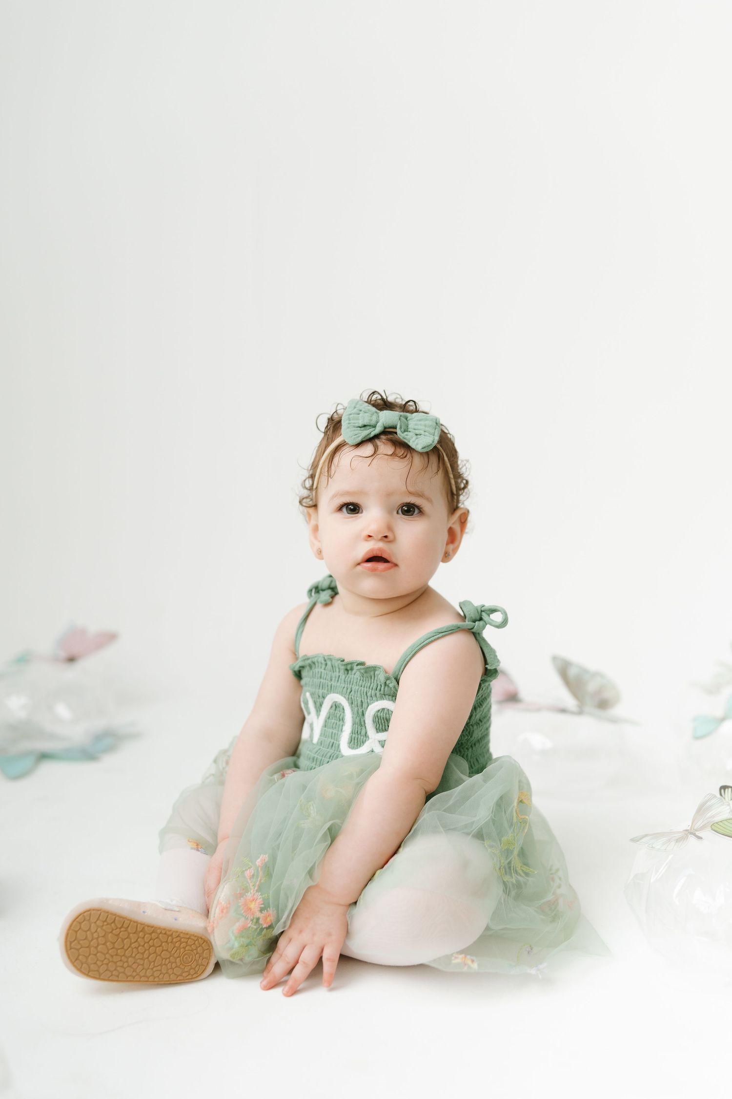 Baby in mint green dress sitting on white backdrop during portrait session.