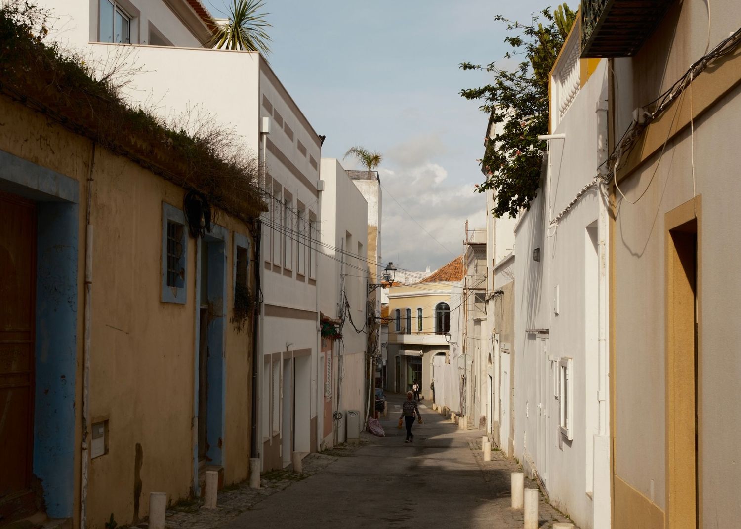 Empty Mediterranean-style street with white walls and blue accents under bright sunlight.
