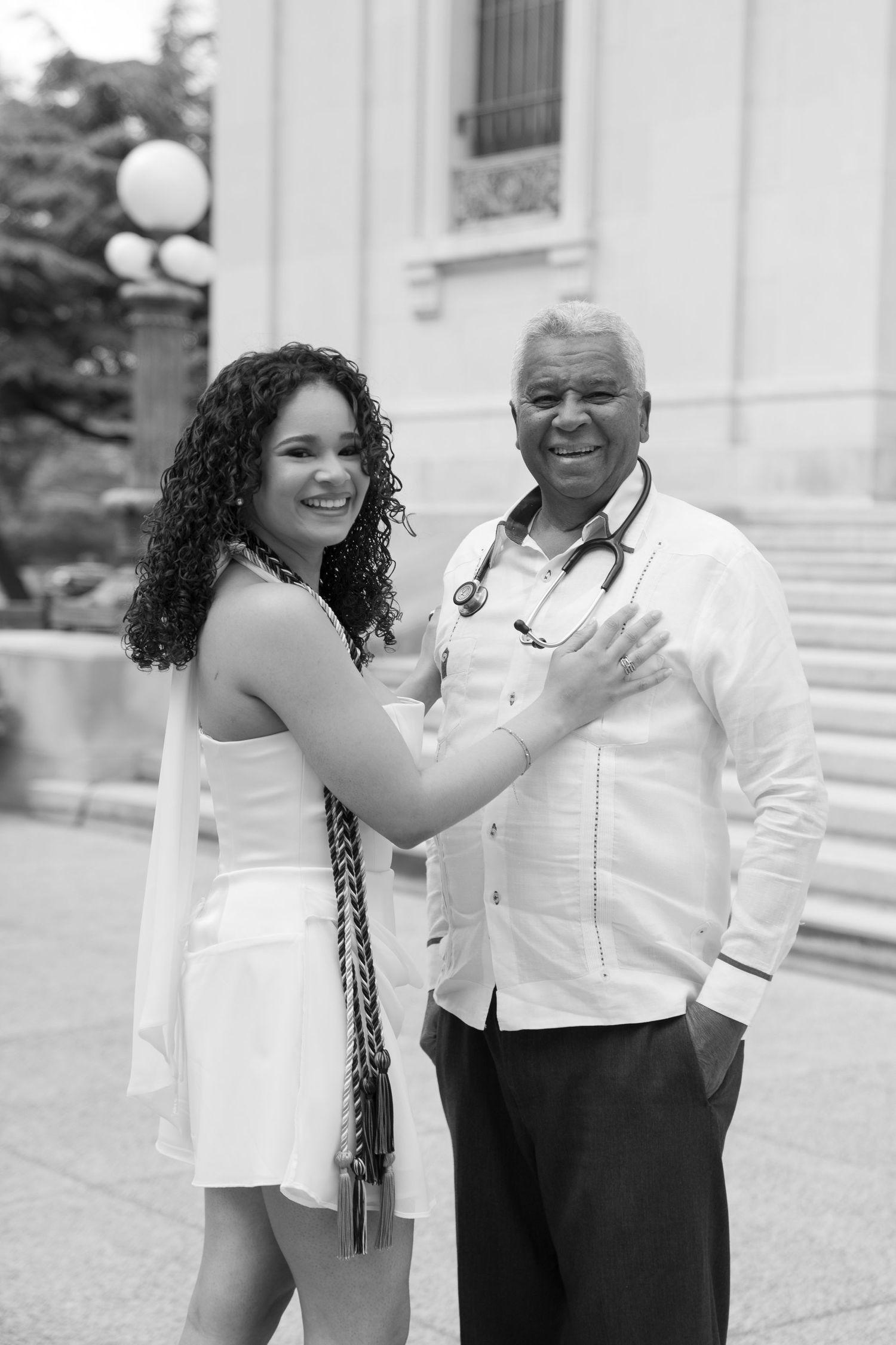Black and white photo of smiling young woman and older man with stethoscope posing together outdoors.