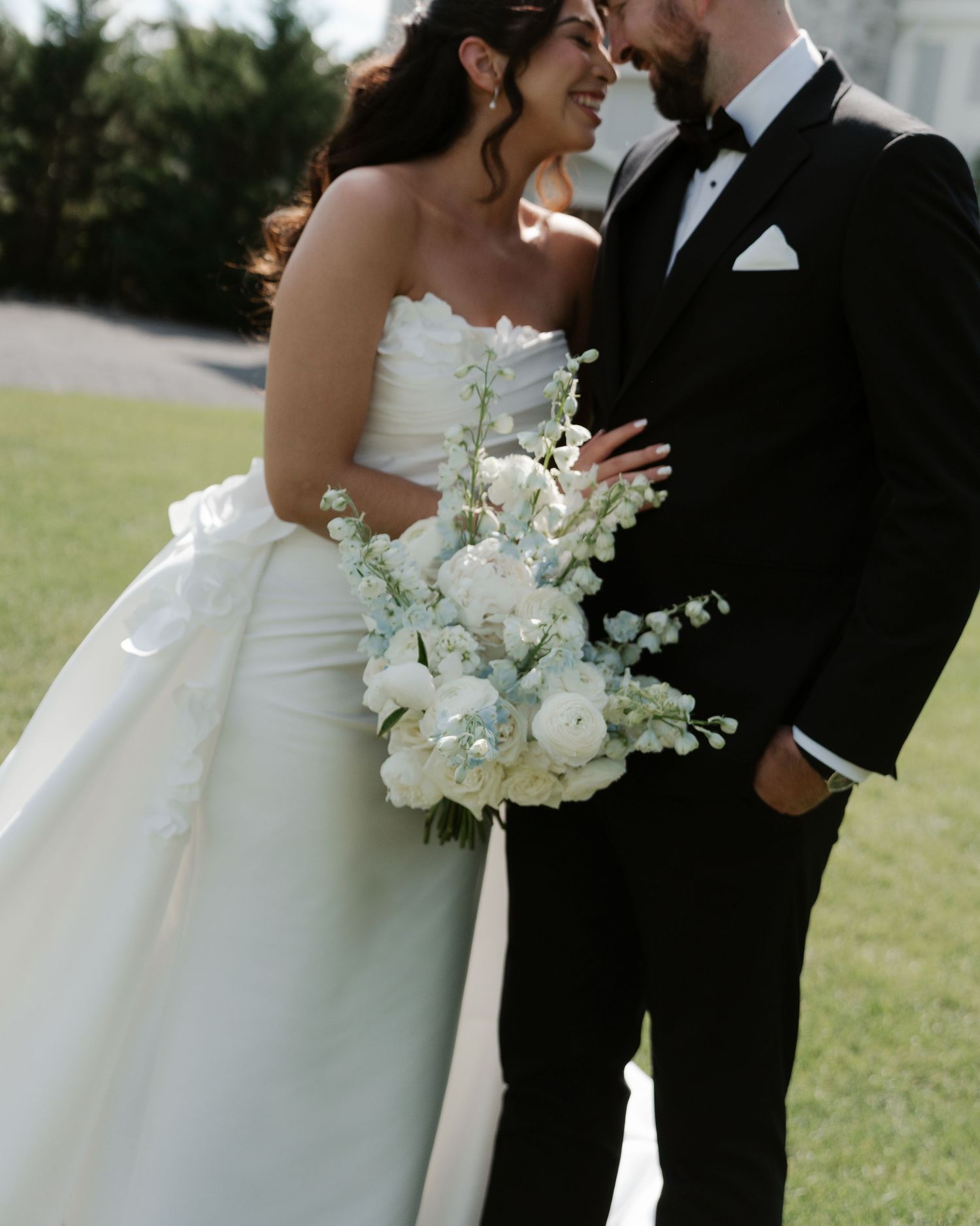 Bride in strapless white ballgown holding white bouquet standing close with groom in black tuxedo.