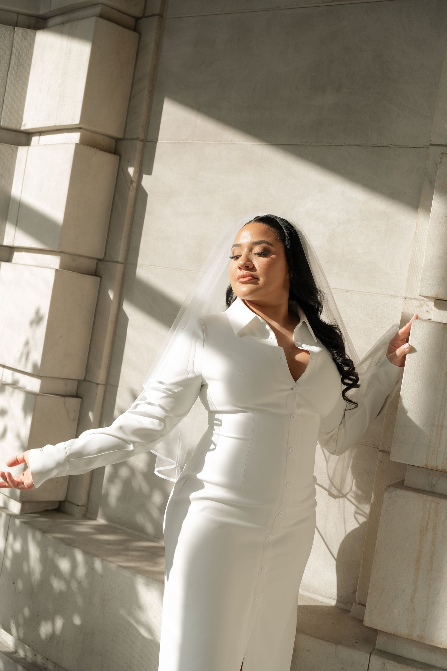A person in an elegant white dress poses gracefully in natural window light.