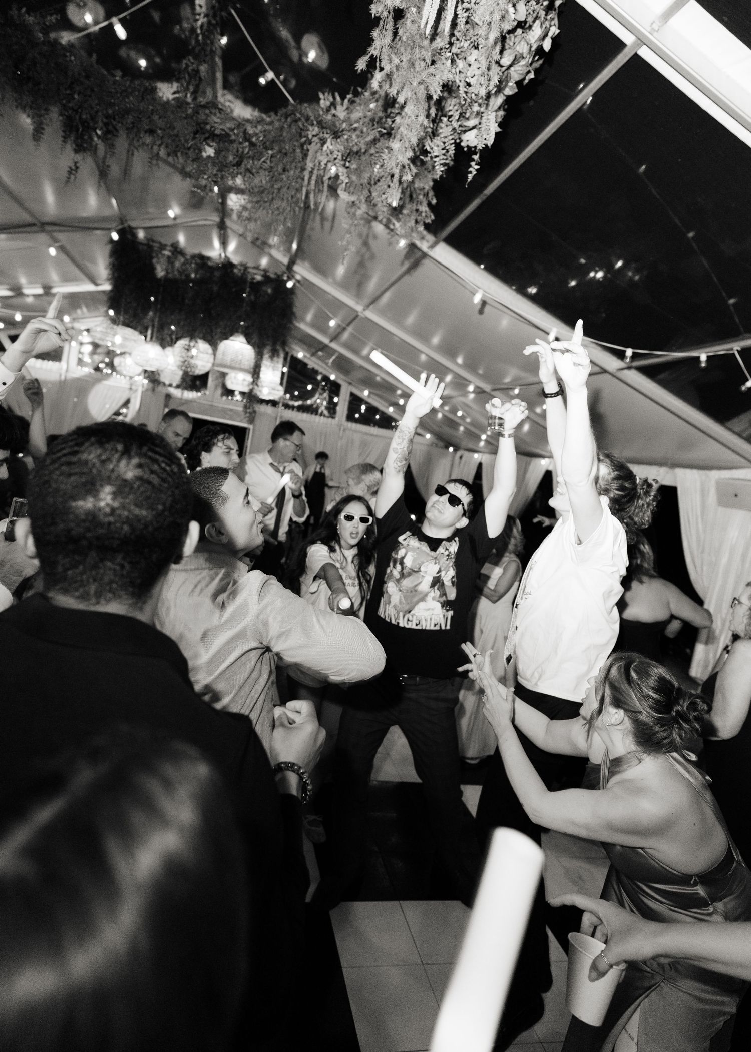 Black and white photo of energetic wedding reception dance party under tent lighting.