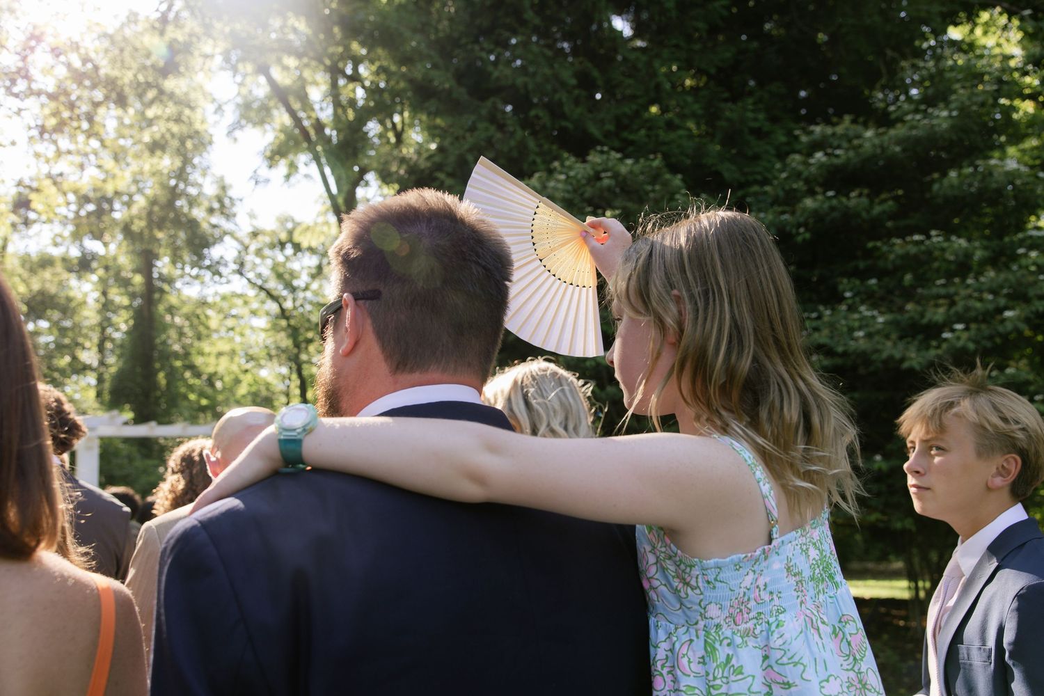 Wedding guests gathering outdoors under trees for celebration.