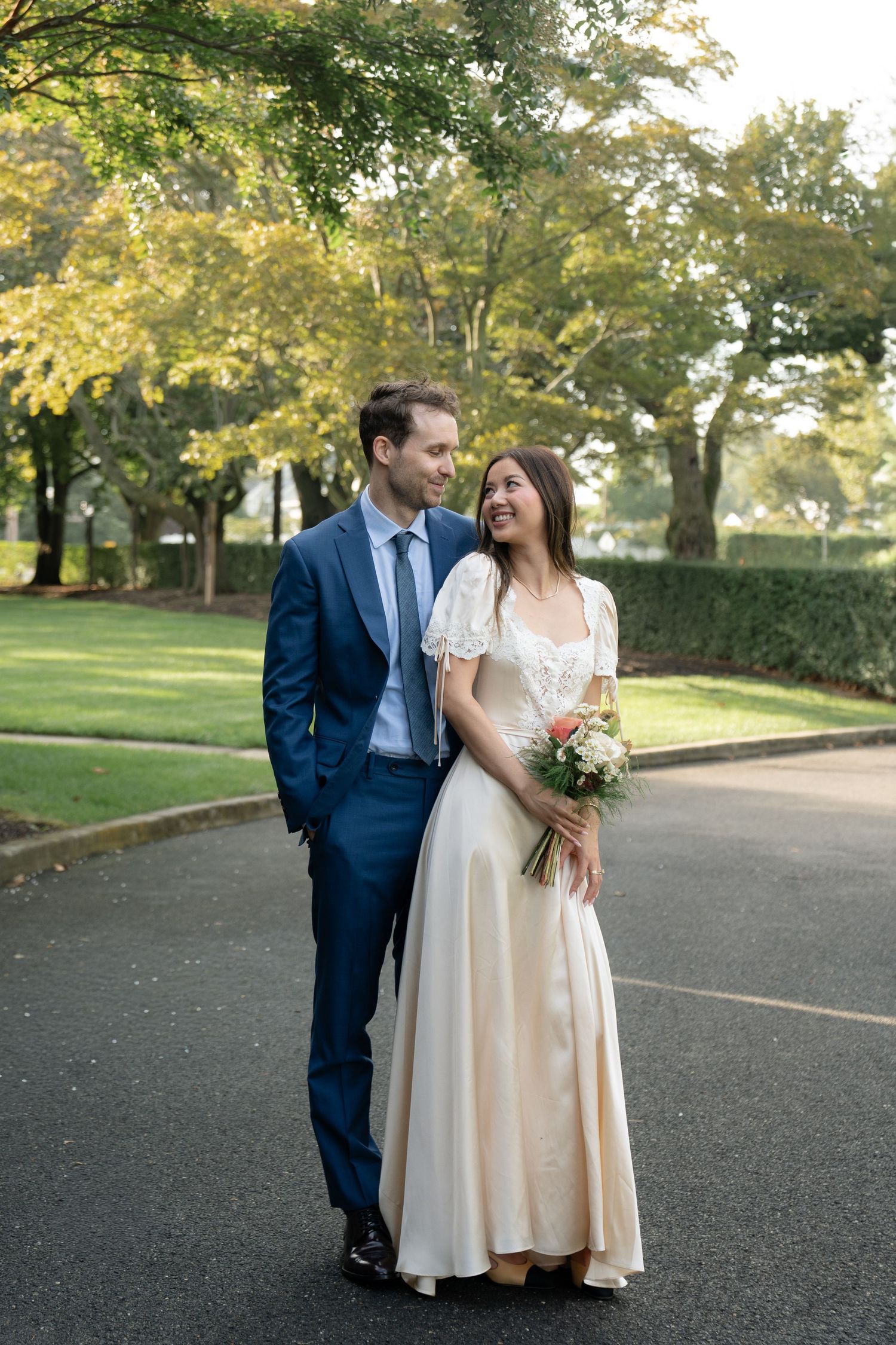 A series of candid wedding moments captured on a paved path surrounded by fall foliage.