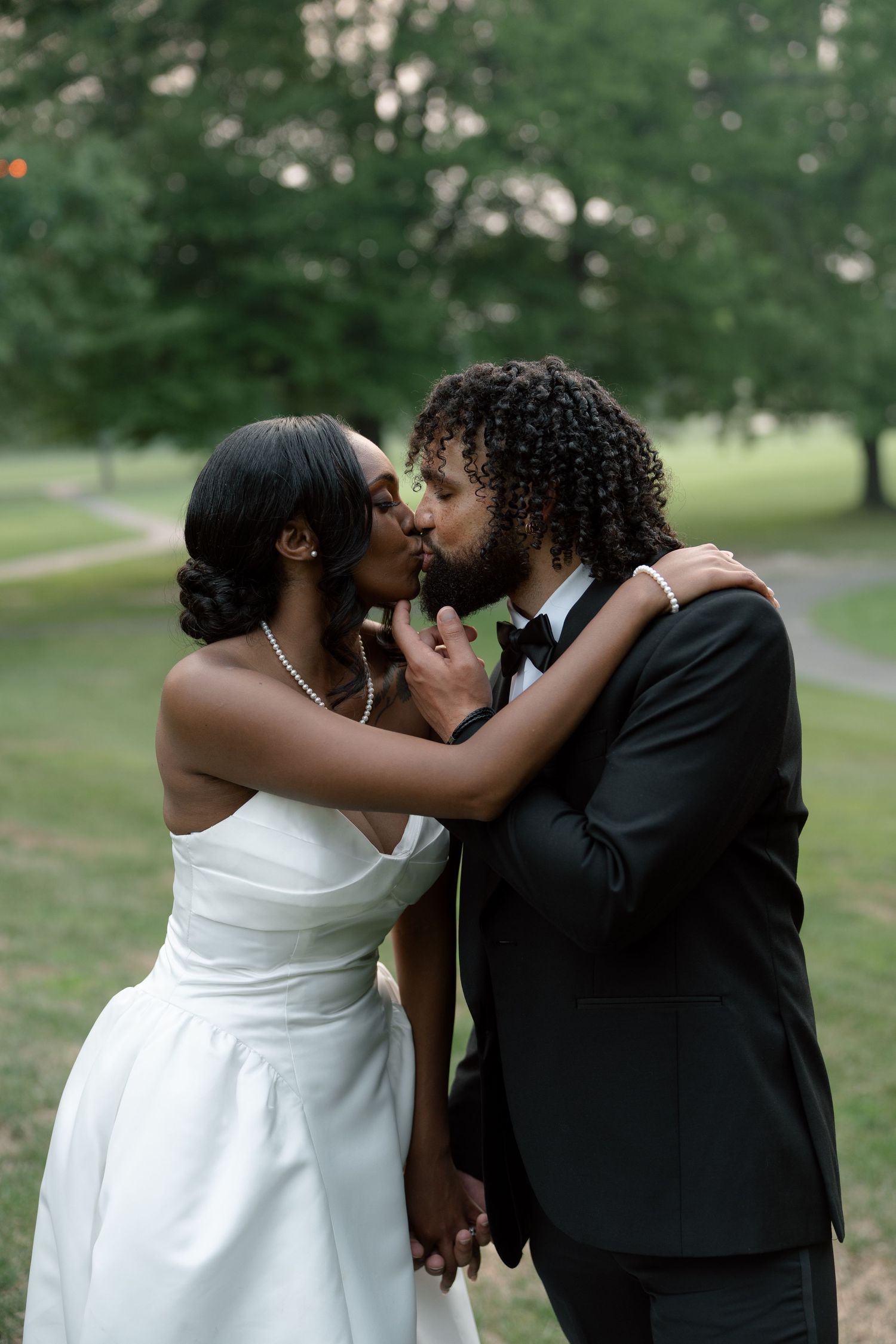 African American bride and groom sharing first kiss outdoors, bride in white gown, groom in black tuxedo.