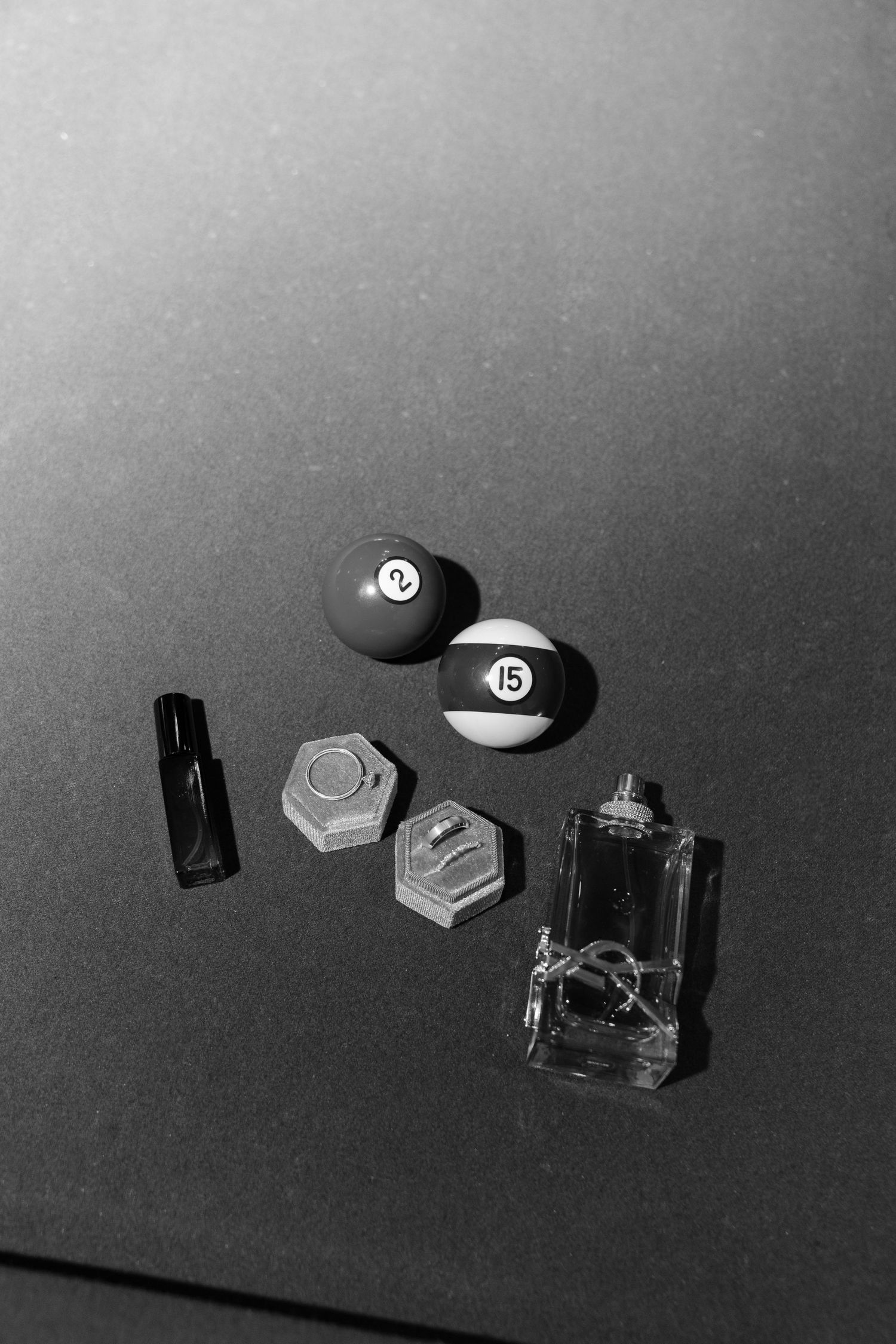 Black and white artistic photograph shows scattered small objects including billiard balls and geometric shapes on a dark surface.
