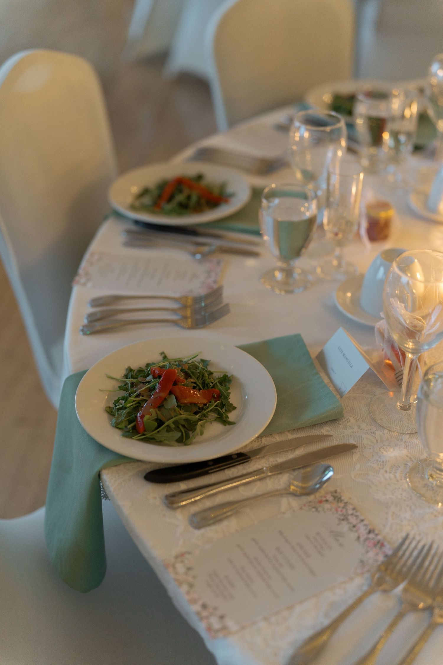 Elegant wedding reception table setting with arugula salads, crystal glassware, and mint green napkins.