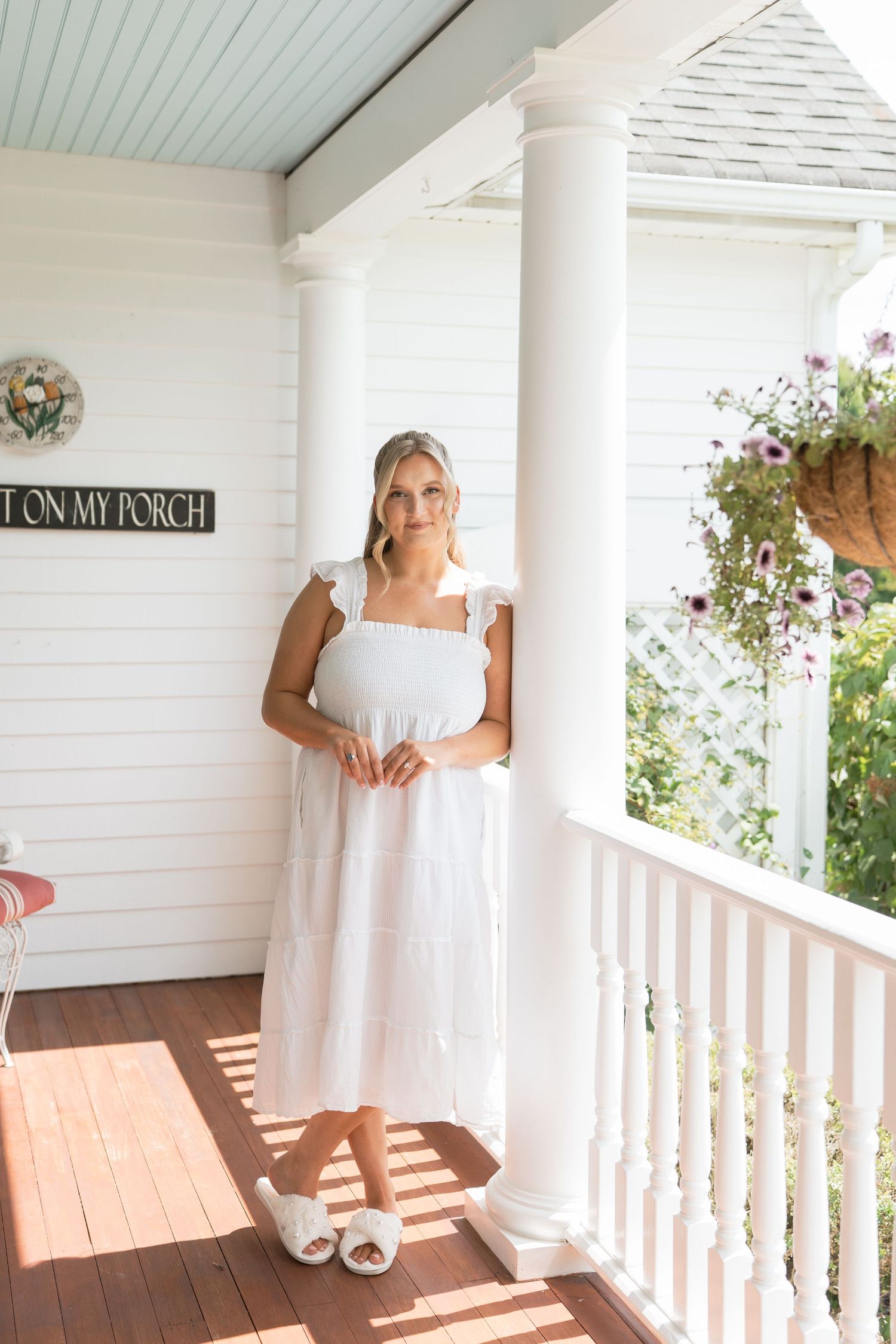 Woman in white midi dress with ruffle straps standing on a white farmhouse porch with columns.