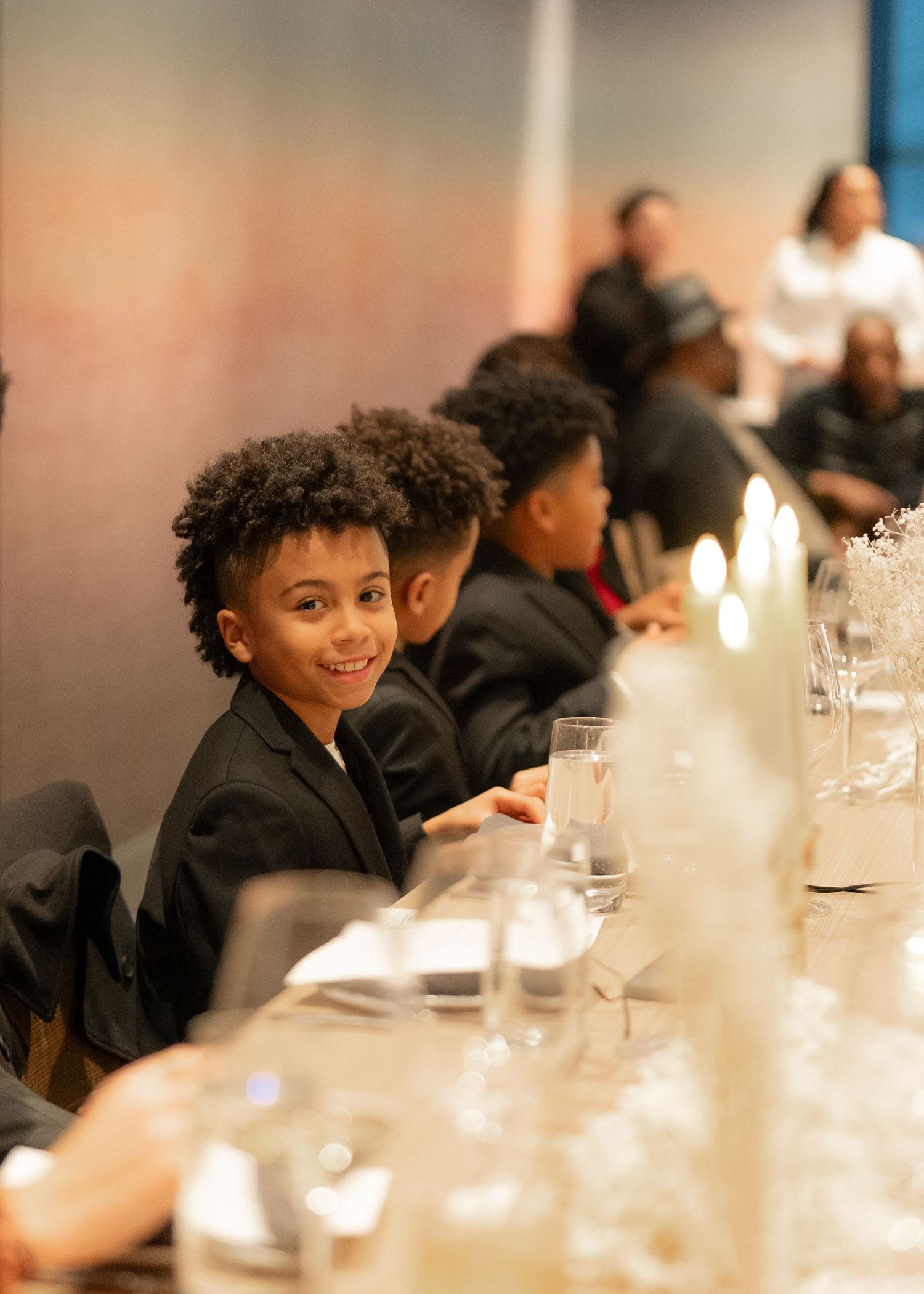 Young guests in formal attire seated at an elegant dinner table with glassware and candles.
