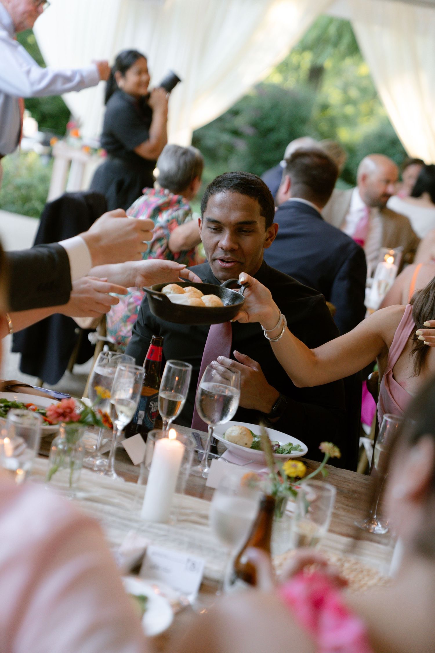 Guests seated at elegant dining tables during a wedding reception pass plates of food and share conversation.