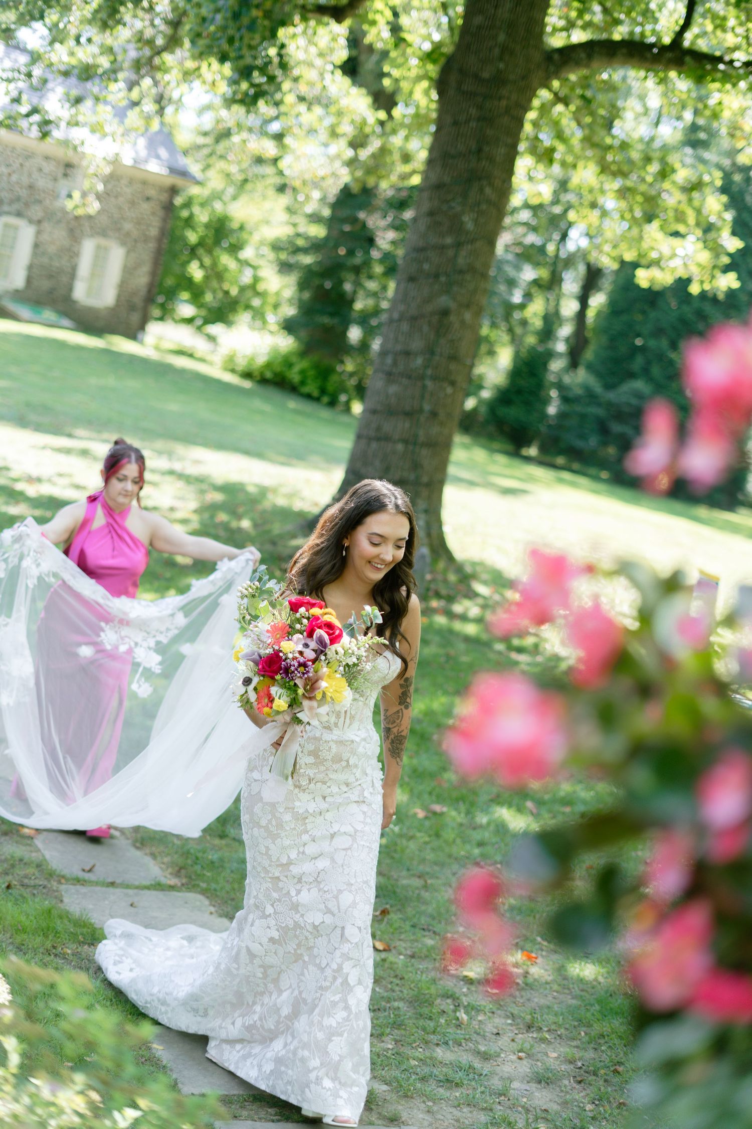 A bride in a white lace dress twirls in a garden setting with pink flowers in bloom.