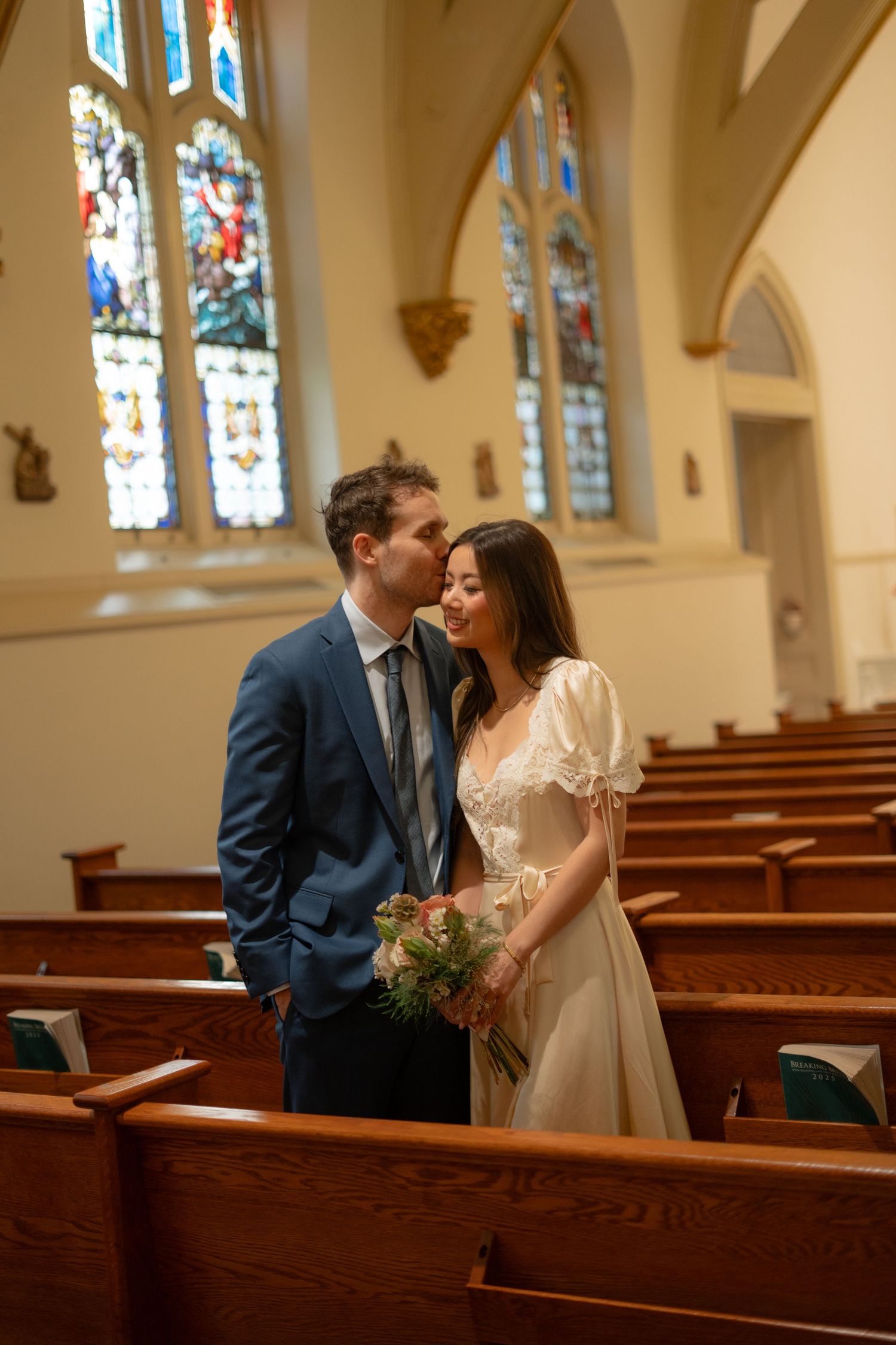 Wedding couple sharing intimate moments in a church with stained glass windows and wooden pews.