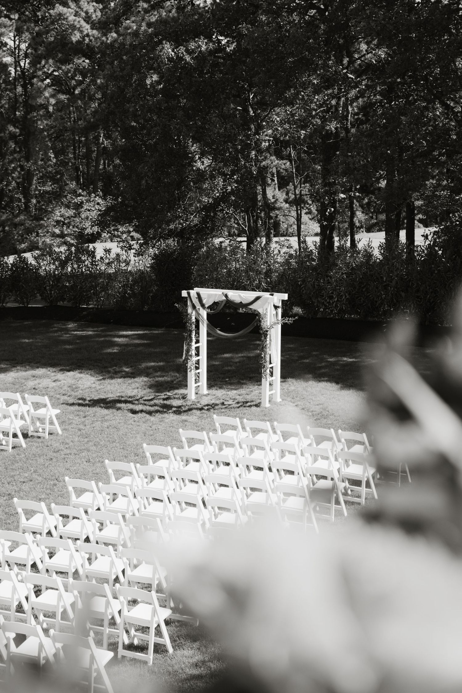 White wedding chairs arranged in rows on grass with decorative arches for an outdoor garden ceremony.