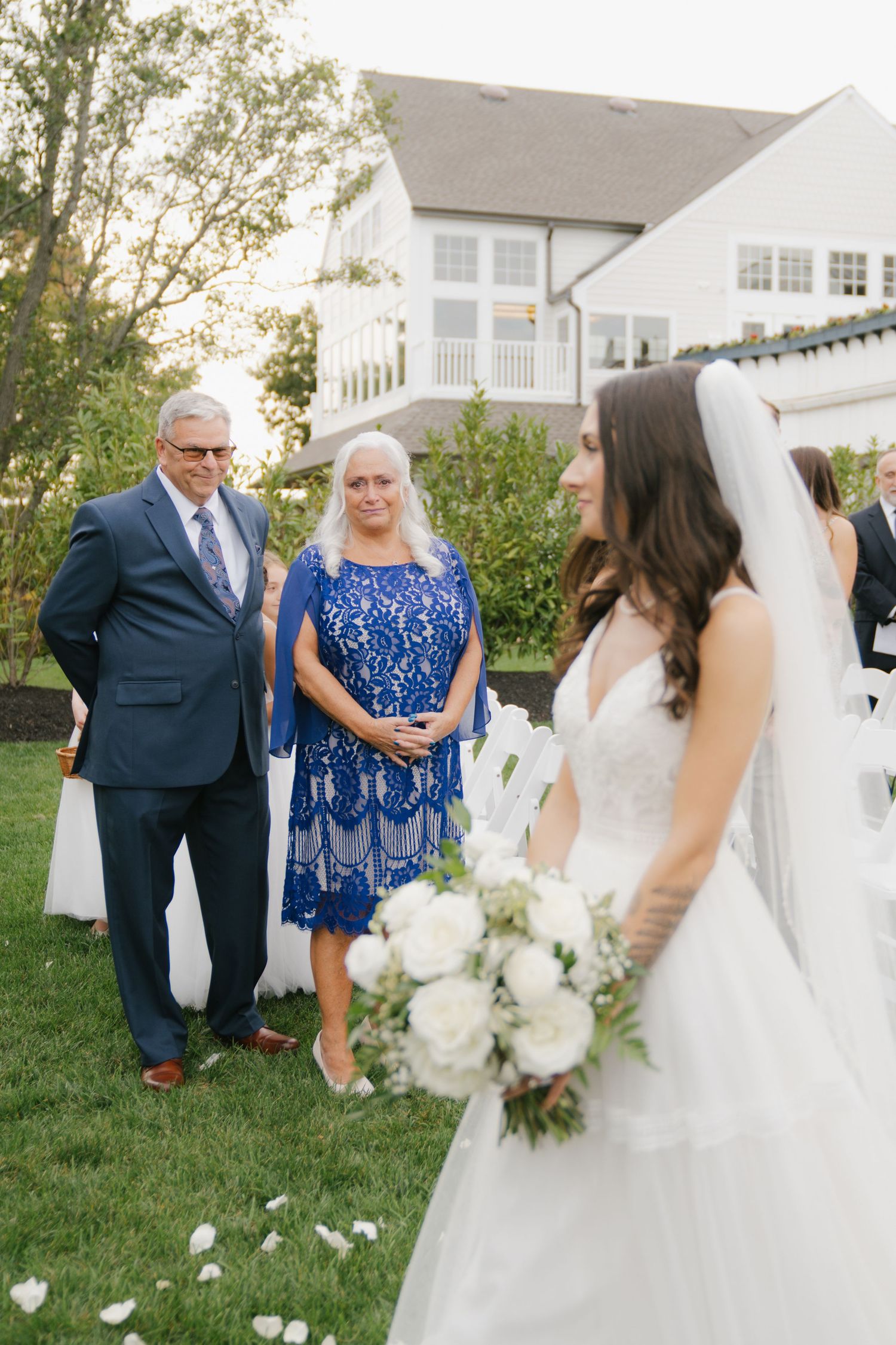 A touching first look moment between family members at an outdoor wedding with white flowers and a blue lace dress.