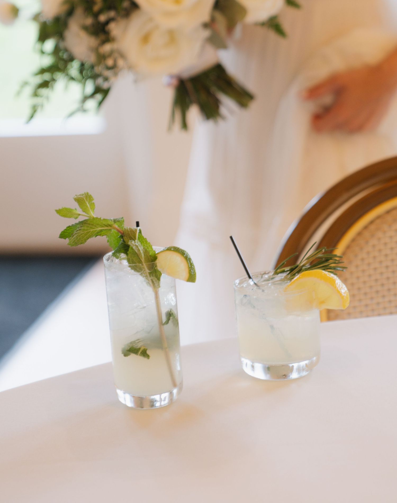 A row of elegant cocktail glasses filled with clear drinks garnished with fresh mint leaves and citrus on a white table.