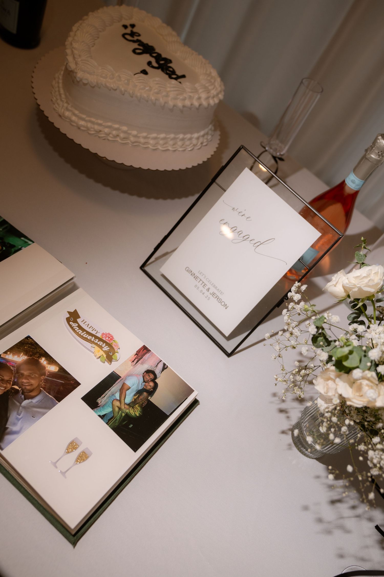 Wedding guest book display with white flowers and framed photos on a table.