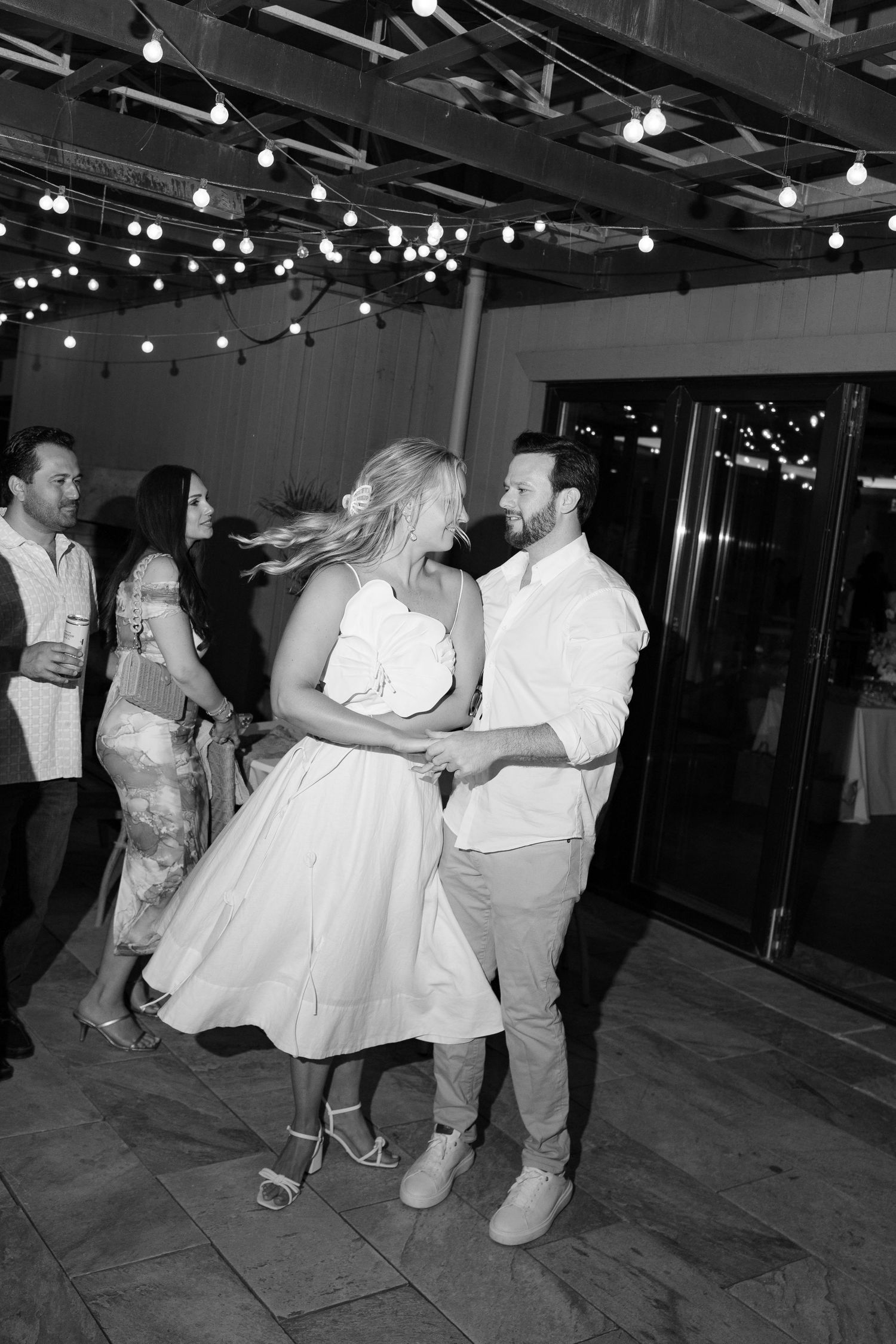 Black and white photo of couples dancing under string lights at an outdoor venue.