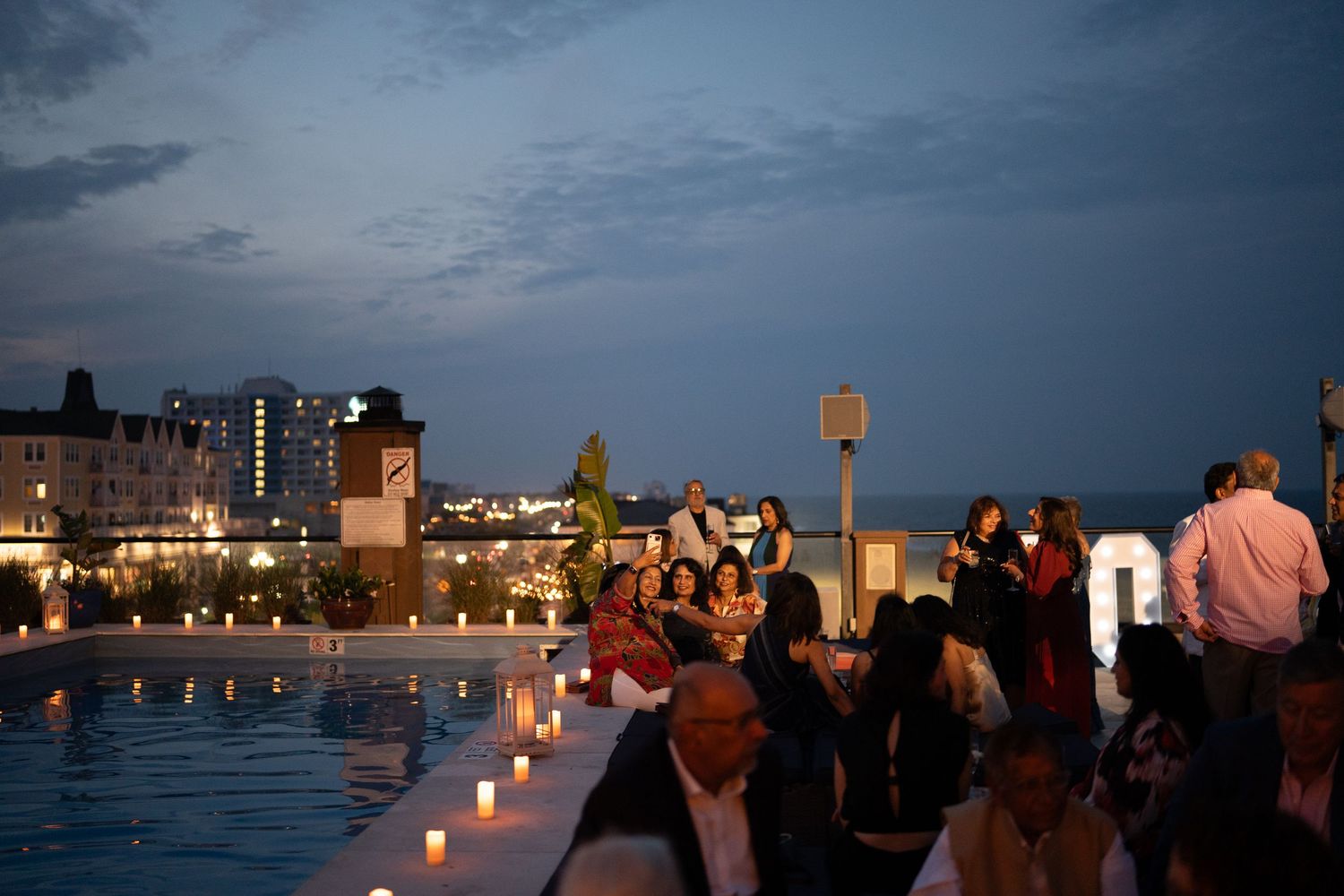 Silhouettes of people gathered at dusk against a waterfront skyline with twinkling lights.