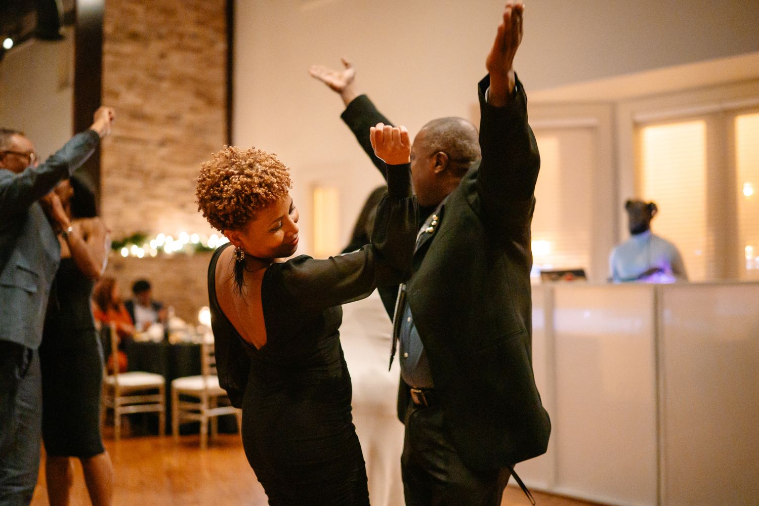 Wedding guests dancing with arms raised in celebration on the dance floor.