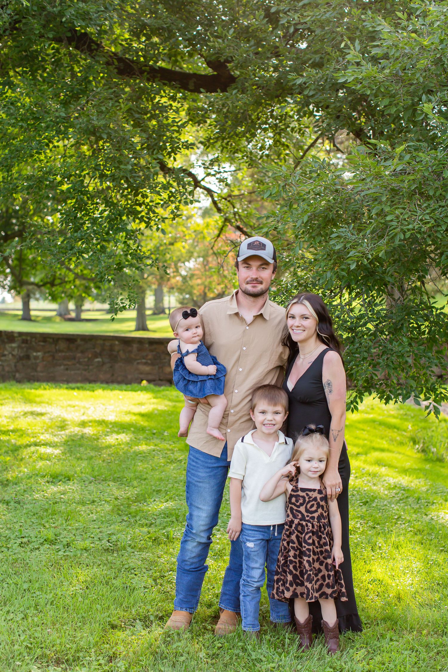 Parents and children posing together on a shaded lawn beneath trees.