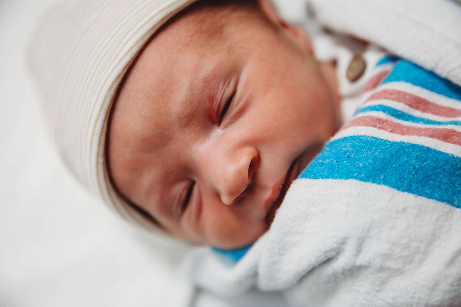 Close-up of a sleeping newborn wrapped in a striped hospital blanket.
