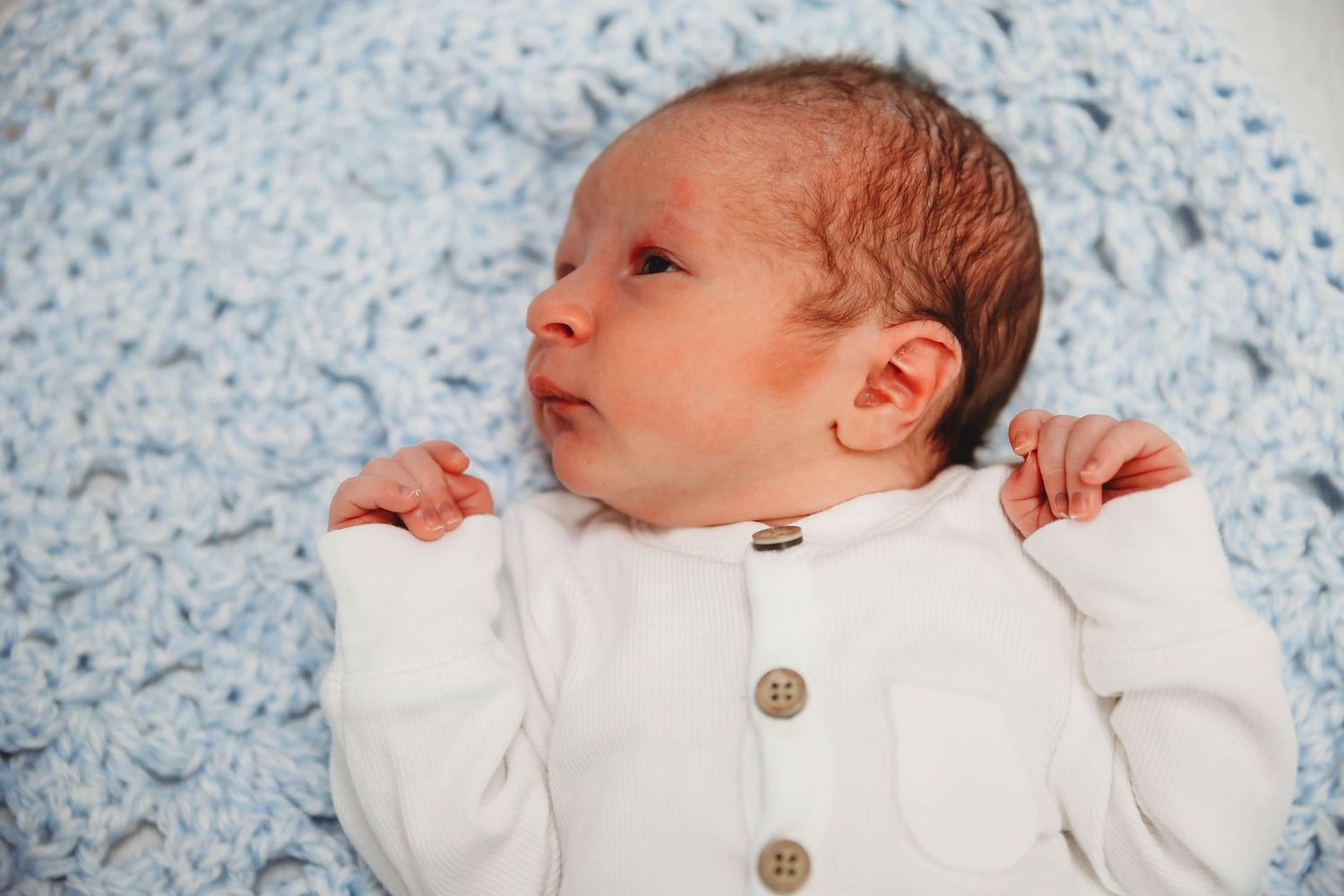 Newborn resting on a pale blue patterned blanket, wearing a white outfit.