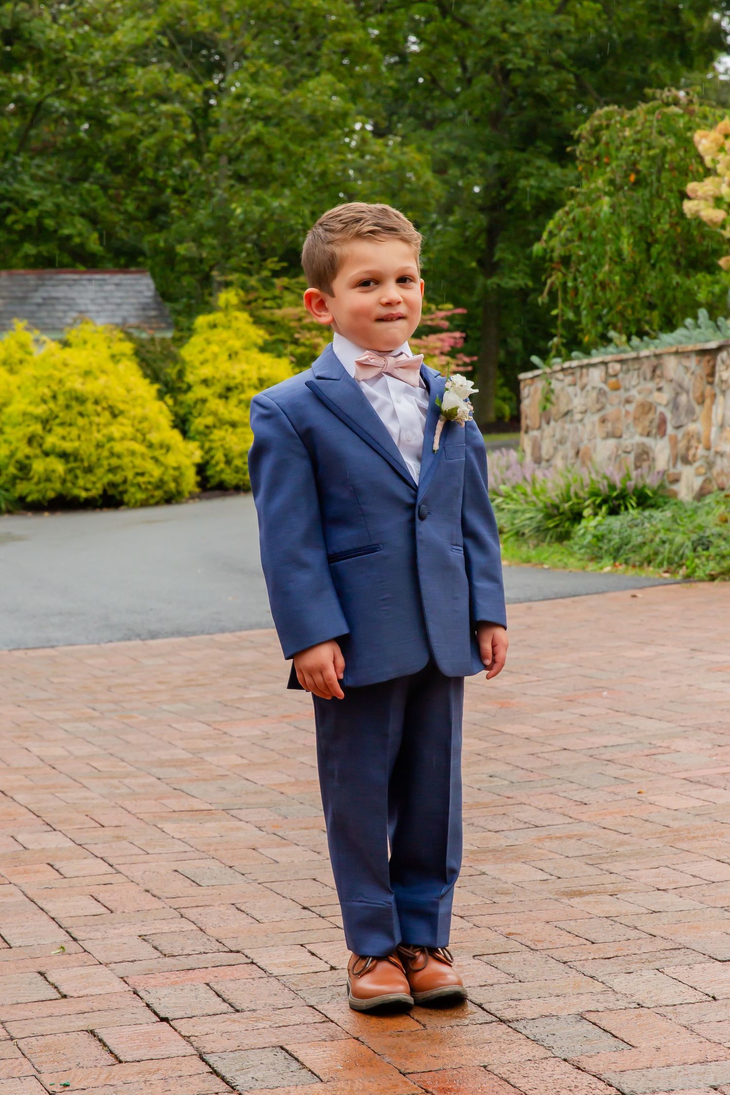 Young boy in a blue suit posing on a brick walkway outdoors.