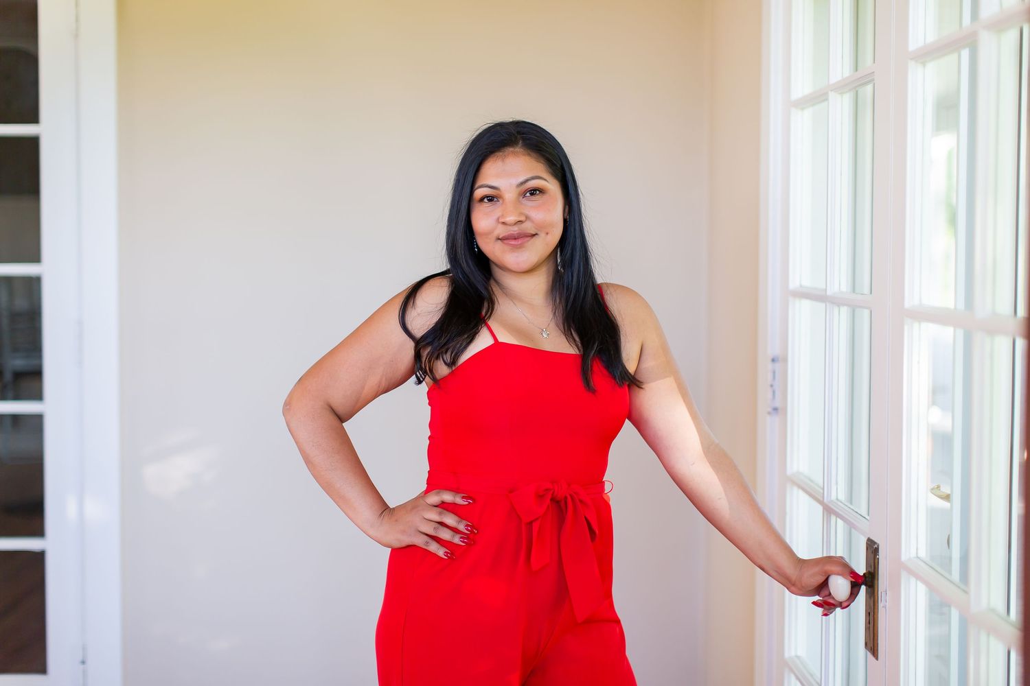Woman in a red outfit standing beside a bright window for a portrait.