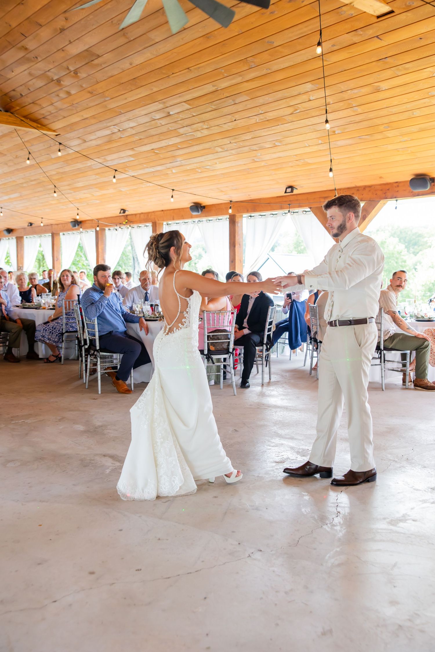 Bride and groom dancing together at their wedding reception beneath a wooden ceiling.
