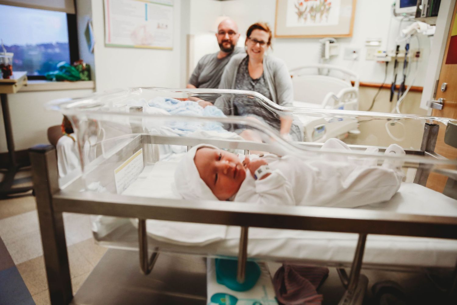 Parents smiling behind their newborn’s hospital bassinet during a Fresh 48 session.