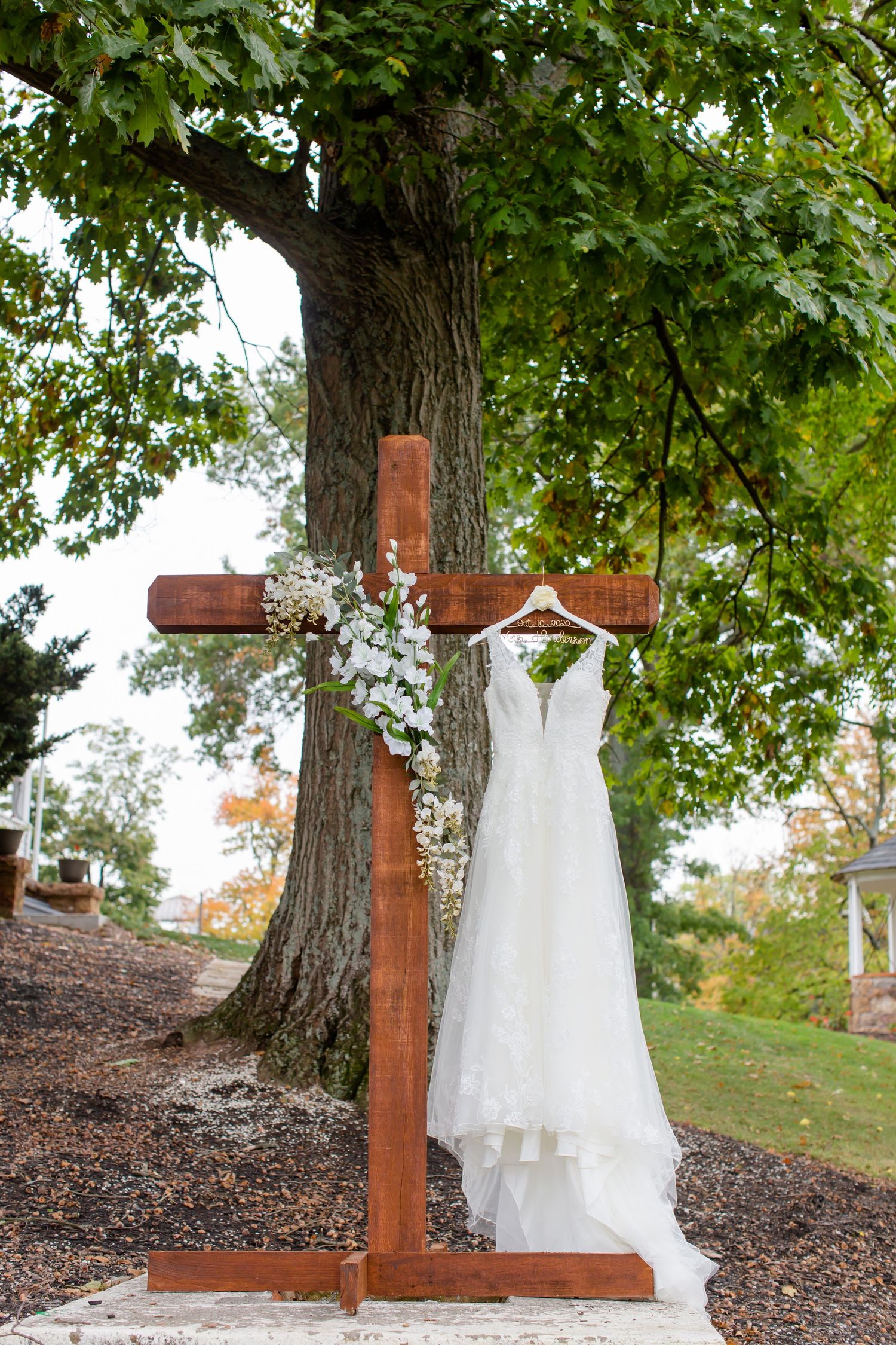 Wedding dress hanging from a wooden stand beneath a tree.